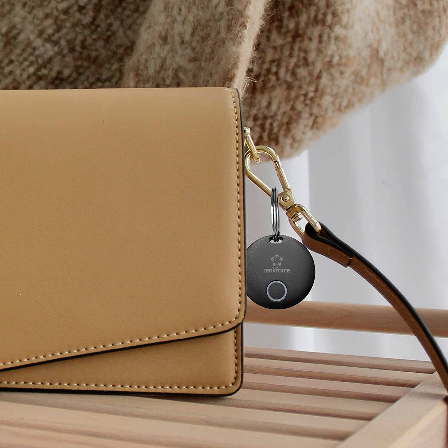 Na drewnianej ławce leży brązowa torebka. U jej boku wisi okrągły czarny brelok z symbolem technologicznym.