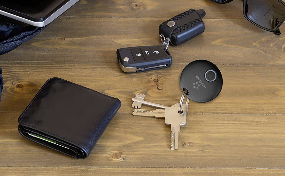 'Pęk kluczy z kluczami i czarnym znacznikiem RFID na drewnianym stole. Obok leży kluczyk samochodowy i czarny portfel.'