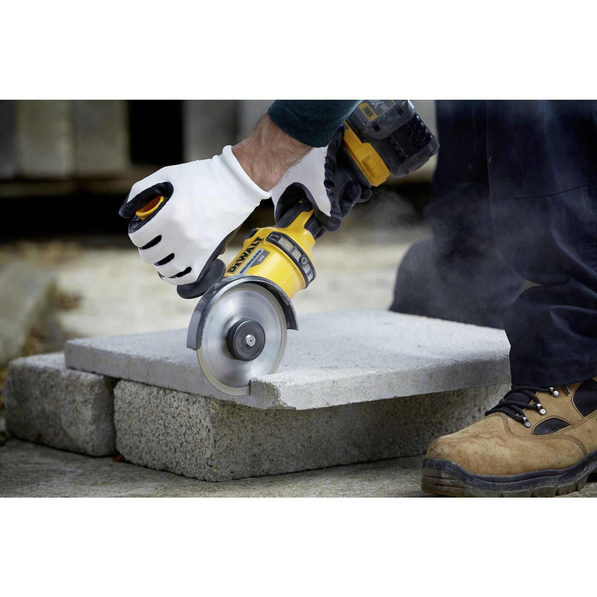 Robotnik przecina blok betonowy elektryczną szlifierką, mając na sobie buty robocze i rękawice ochronne.
