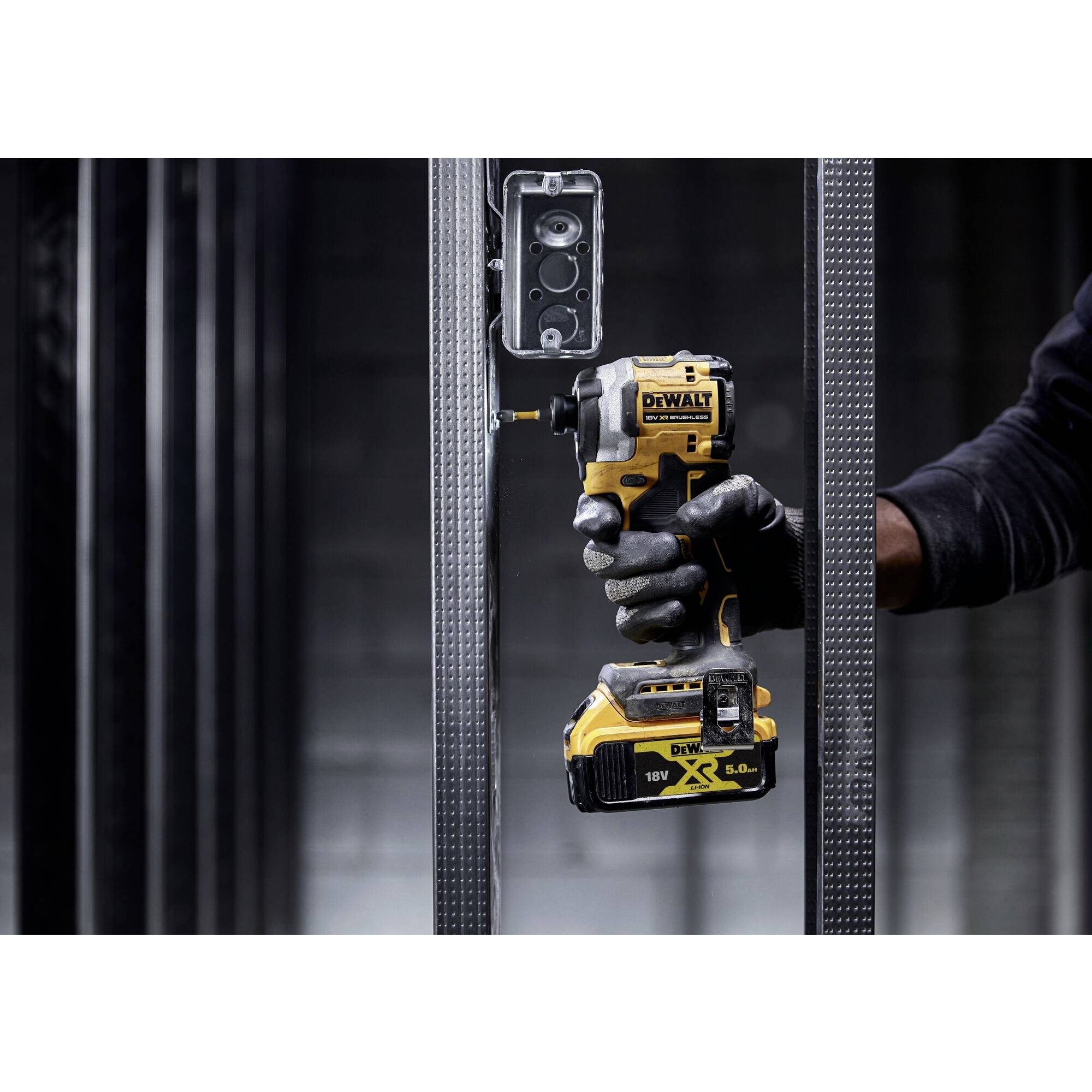 Osoba mocuje obudowę elektryczną do metalowego stojaka za pomocą wkrętarki akumulatorowej. Narzędzie i czynność robocza są w centrum uwagi.