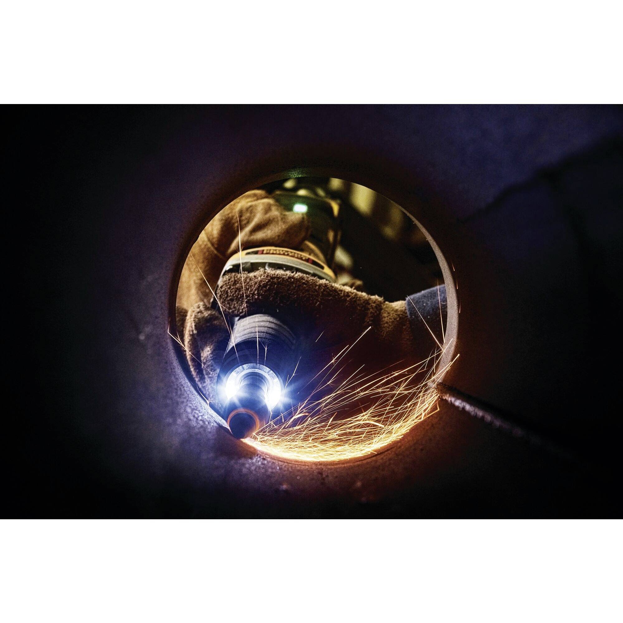 Robotnik spawający w ciemnej rurze, lecące iskry. Widoczna odzież ochronna i rękawice.