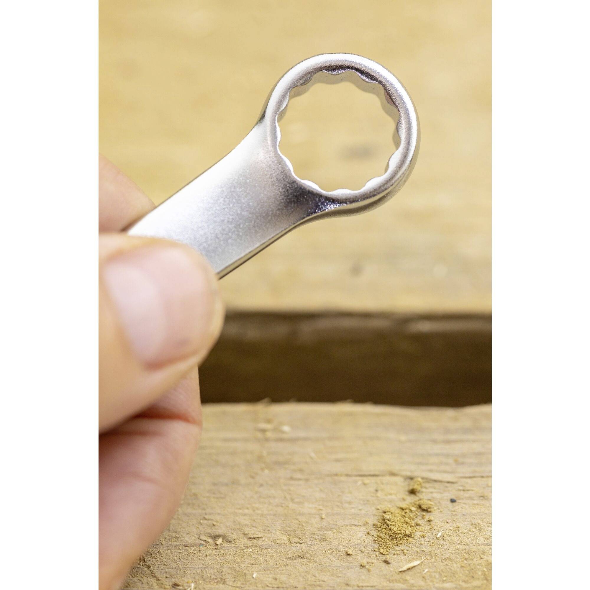 Dłoń trzyma srebrny otwieracz do butelek nad drewnianym stołem. Tło jest rozmyte.