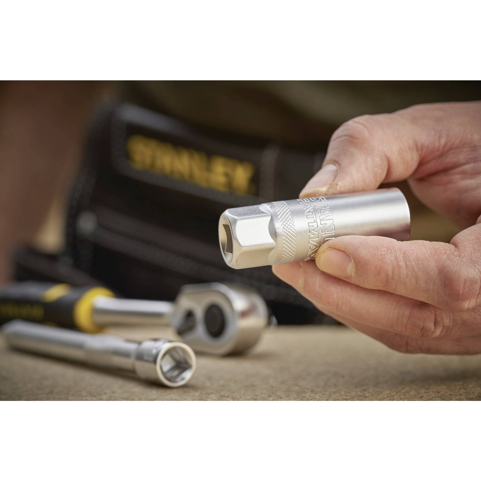 Osoba trzyma srebrny kołek przed rozmytym tłem z dodatkowymi narzędziami na warsztacie.