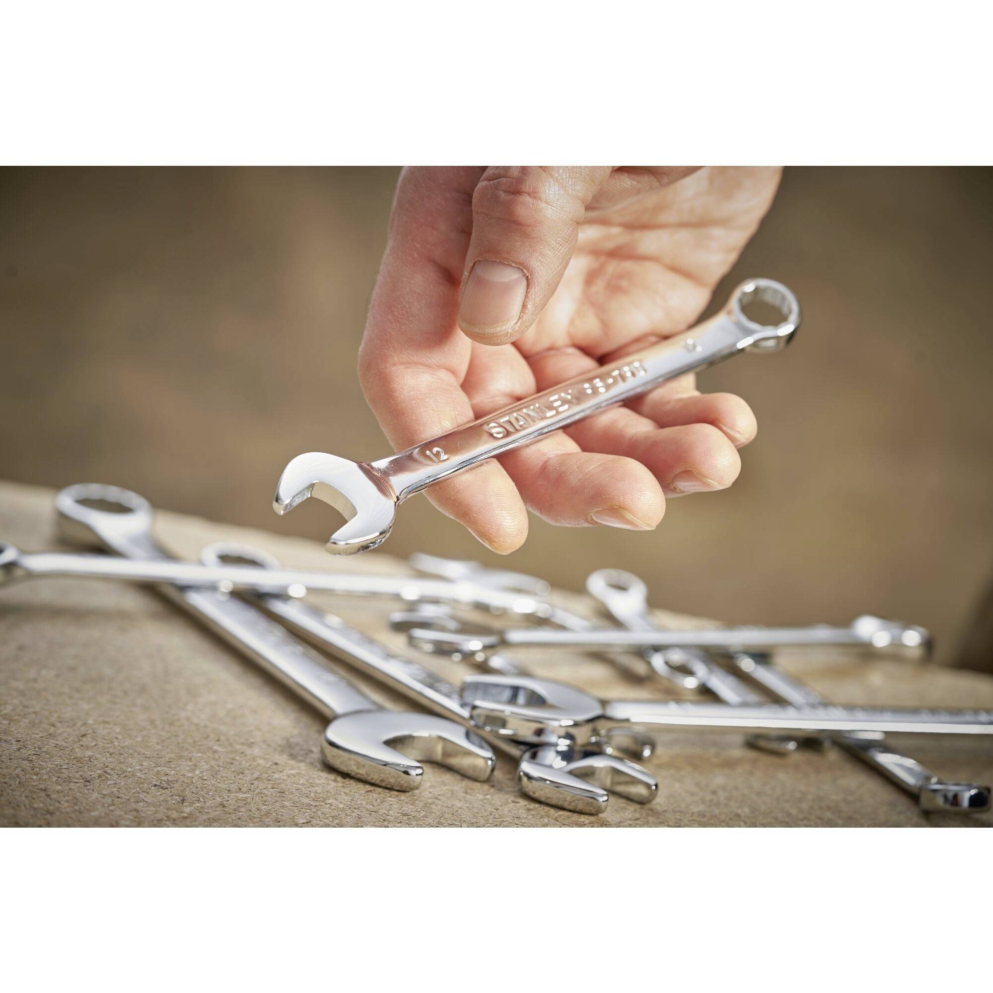 Jedna ręka trzyma lśniący klucz nastawny nad stołem z kilkoma innymi kluczami nastawnym.