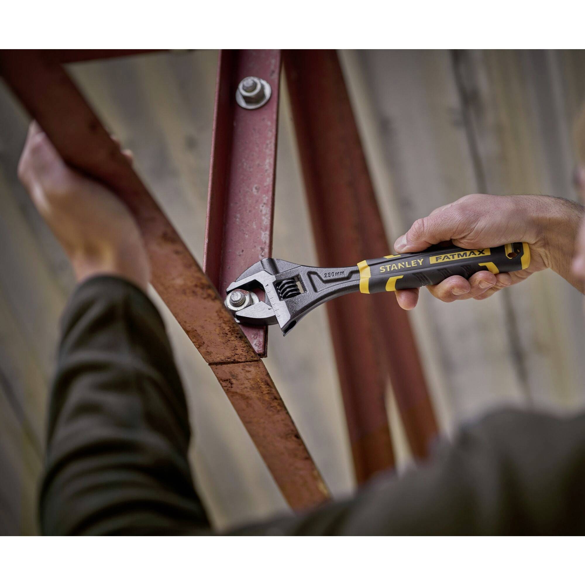 Osoba dokręca śrubę na metalowej belce regulowanym kluczem nastawnym.