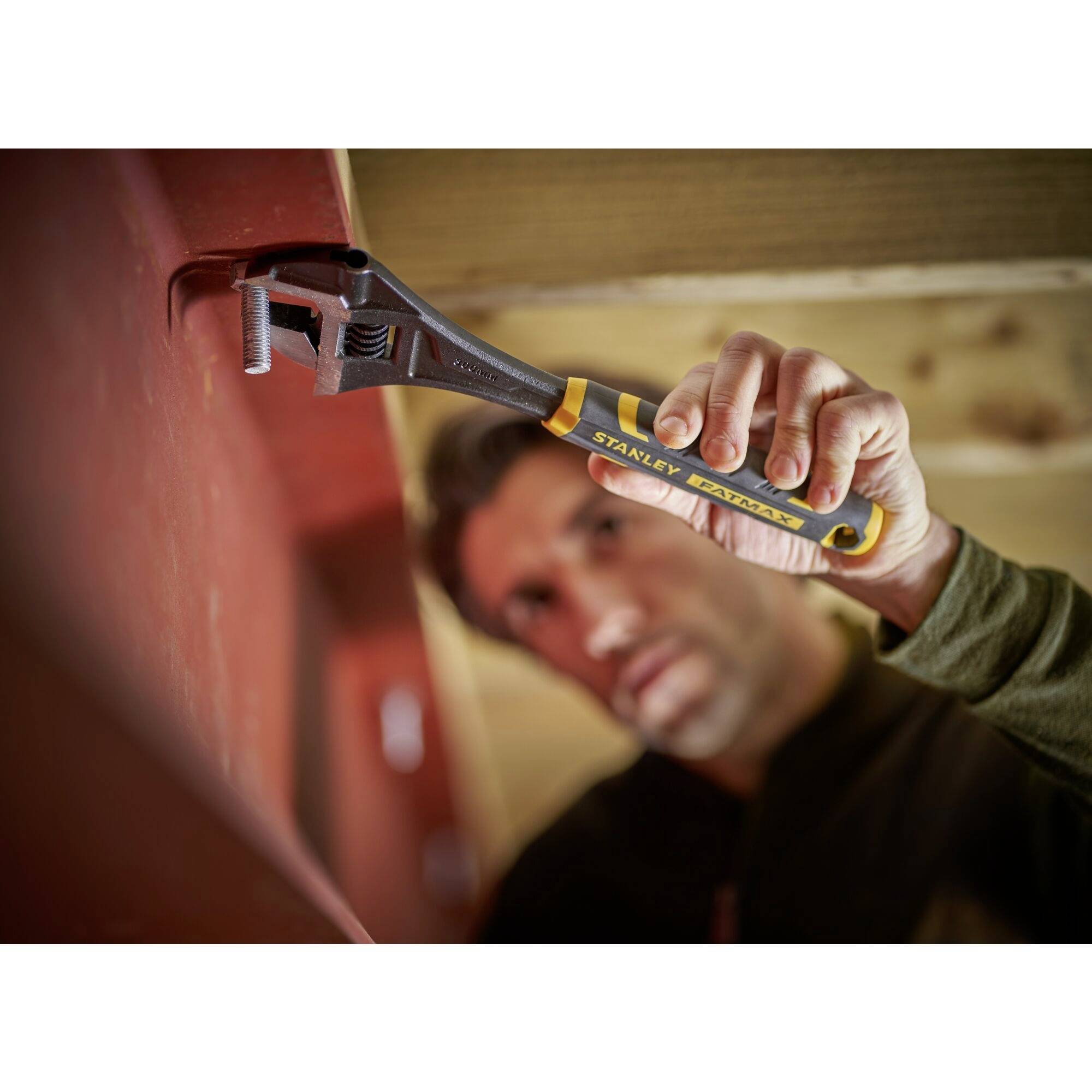 Osoba używa klucza nastawnego, aby dokręcić śrubę w drewnianym belkowaniu.