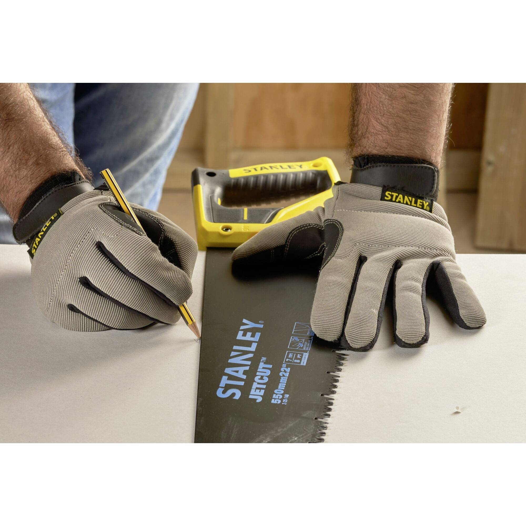 Osoba w rękawiczkach rysuje ołówkiem na desce drewnianej. Obok leży piła Stanley'a.