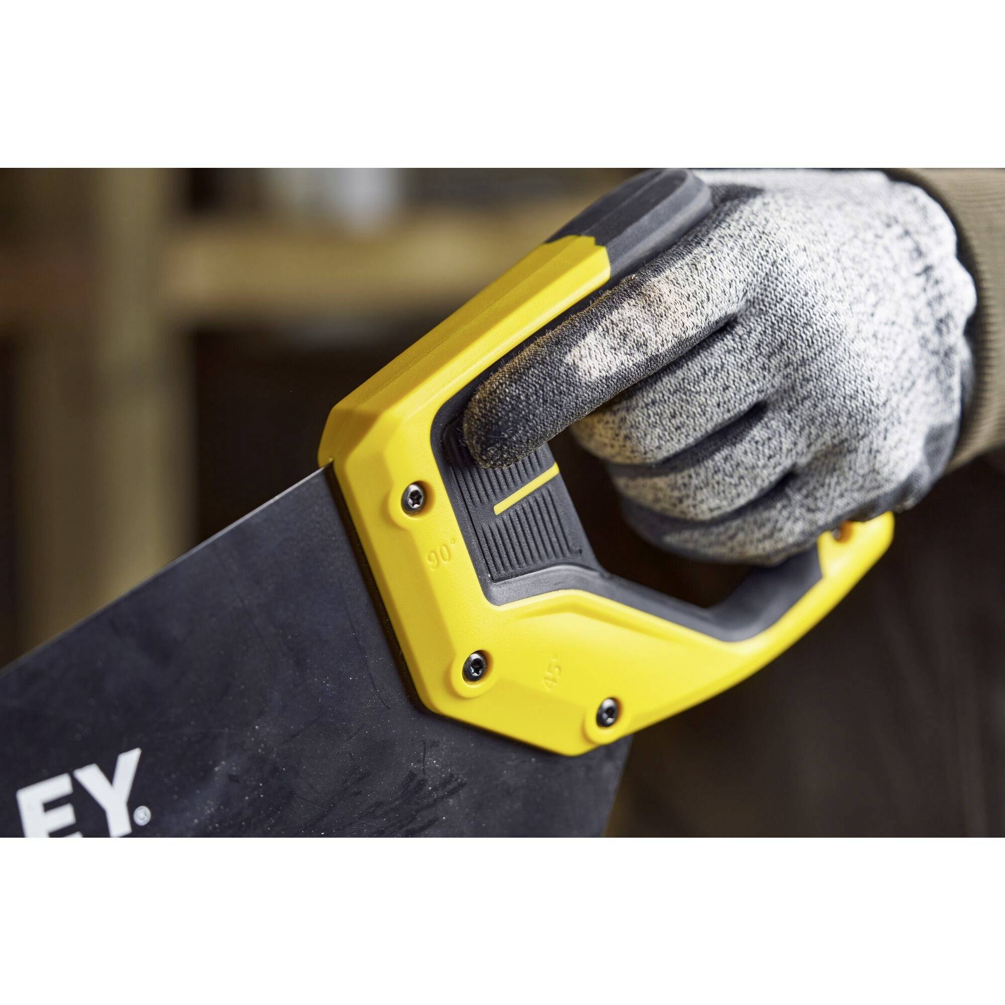 Osoba w rękawicach roboczych trzyma piłę z żółtą rękojeścią, gotowa do pracy.