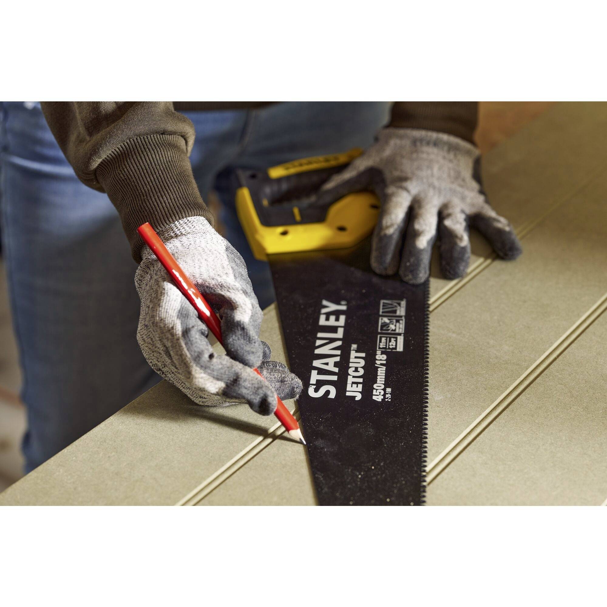 Osoba trzyma piłę ręczną i zaznacza linię czerwonym mazakiem na desce drewnianej.