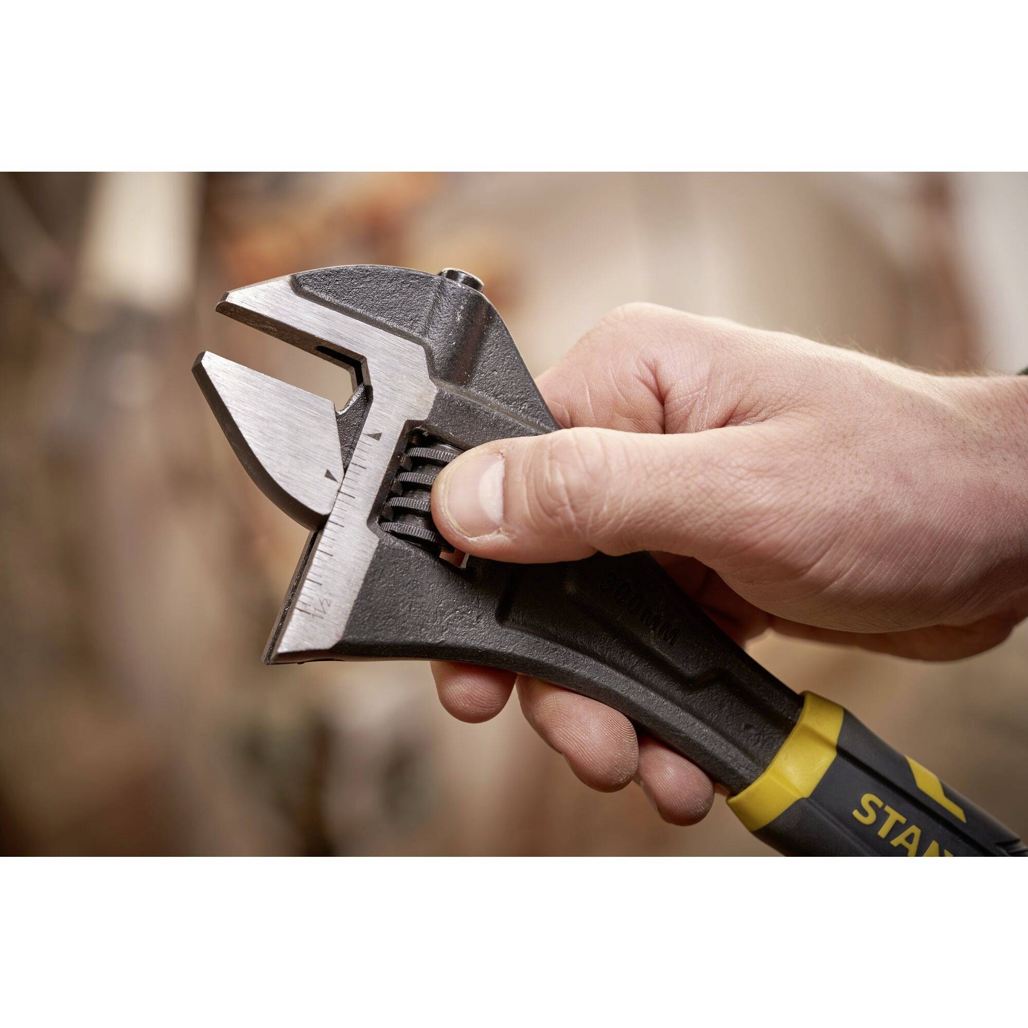 Jedna ręka trzyma regulowany klucz nastawny na niewyraźnym tle. Klucz jest rozwarty.