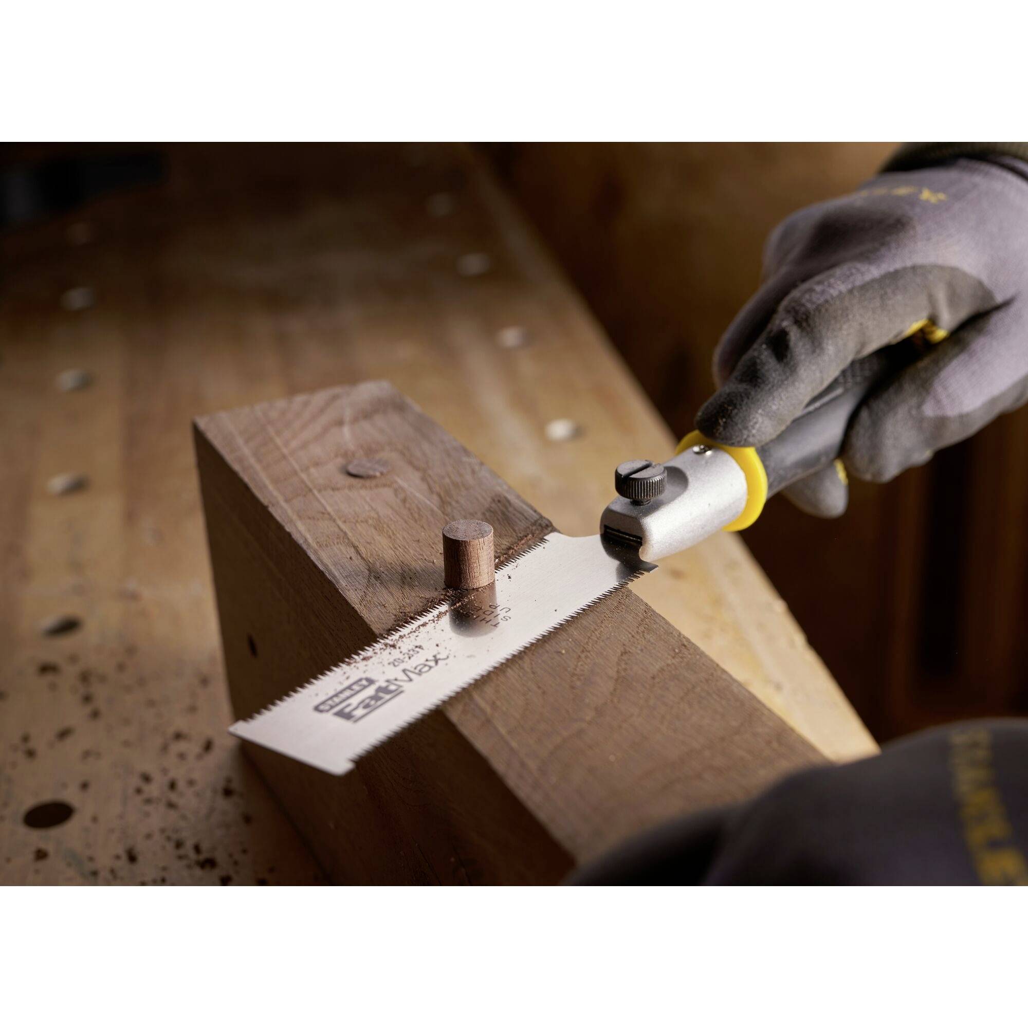 Osoba w rękawicach roboczych ucina drewniany kołek równo z dużym blokiem drewna za pomocą piły do drewna.