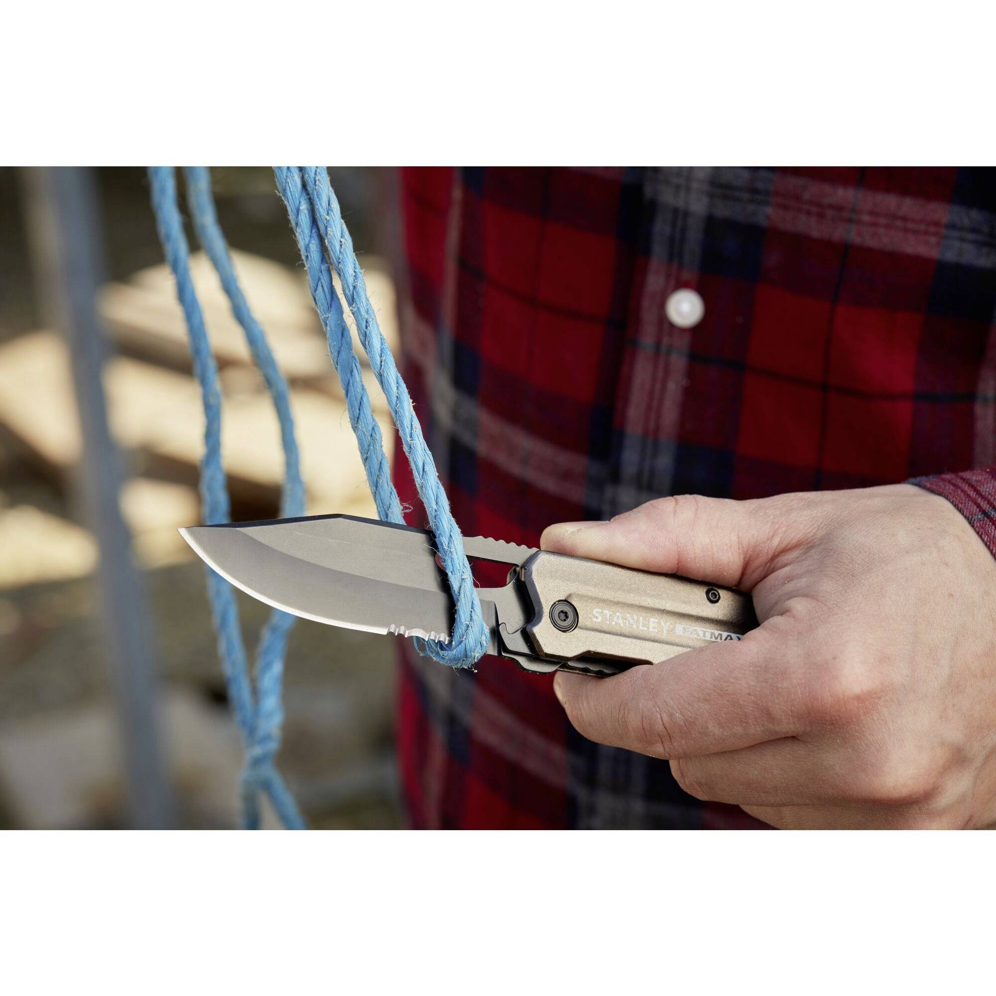 Mężczyzna przecina niebieską linę scyzorykiem. Ma na sobie koszulę w czerwoną kratę. W tle widoczne są metalowe struktury.