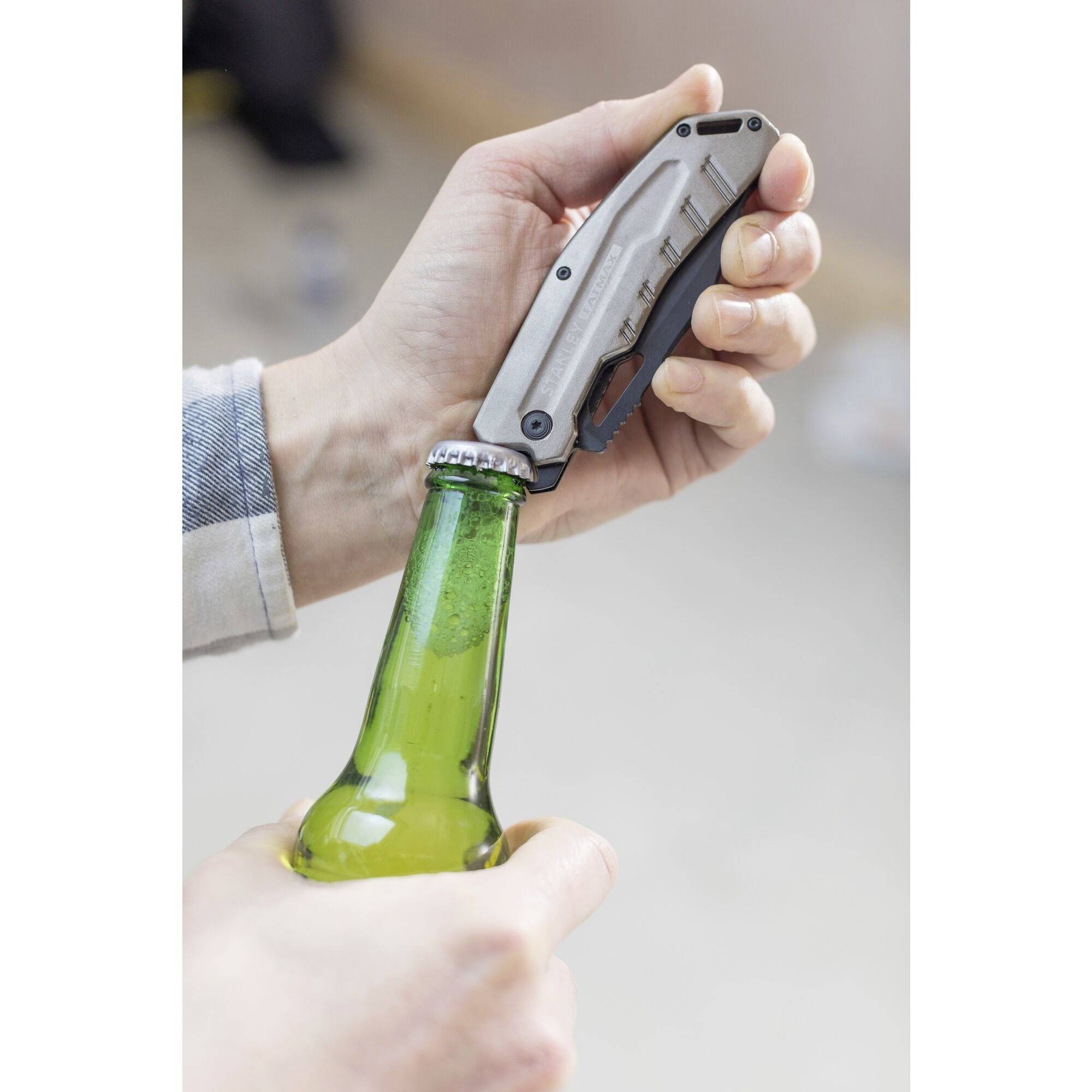 Ręka otwiera zieloną butelkę scyzorykiem.