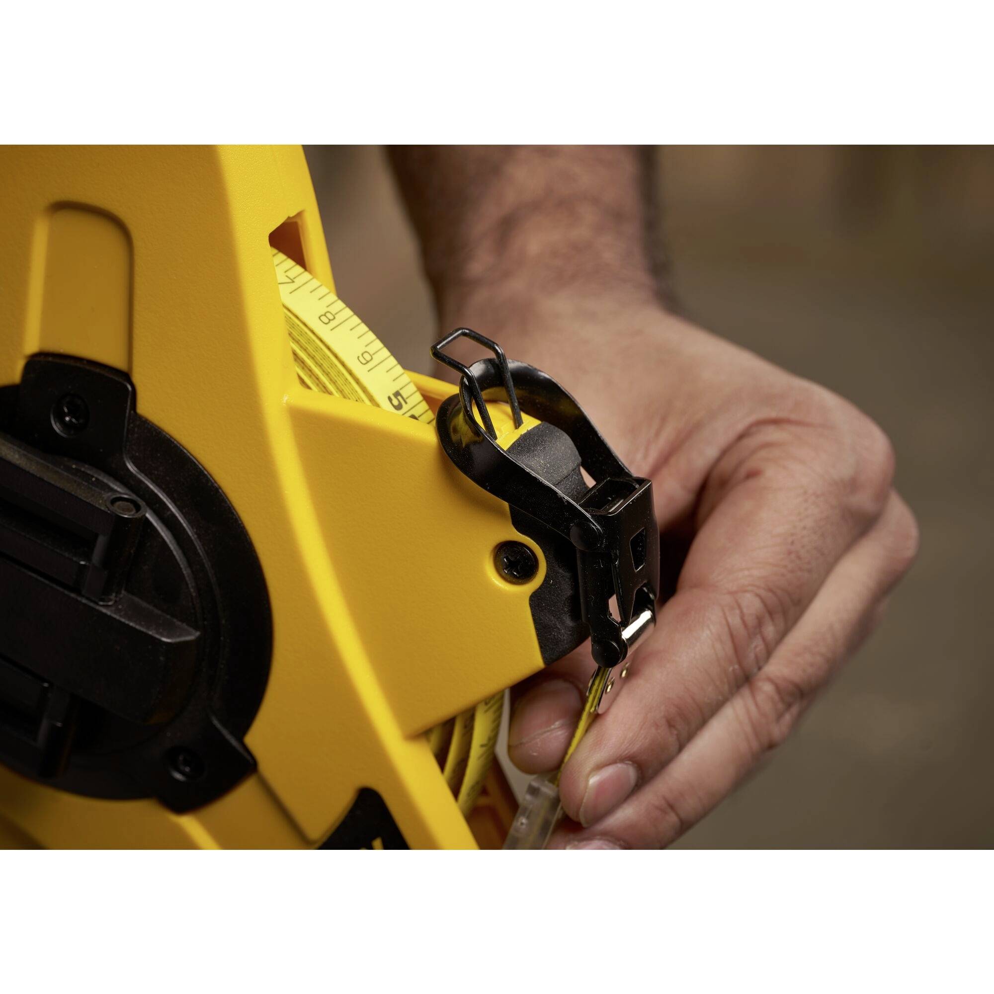 Dłoń trzyma żółty miarodajny miarkę z czarnym klipsem. Miarka jest wyciągana z żółtej obudowy i pokazuje numery w centymetrach.