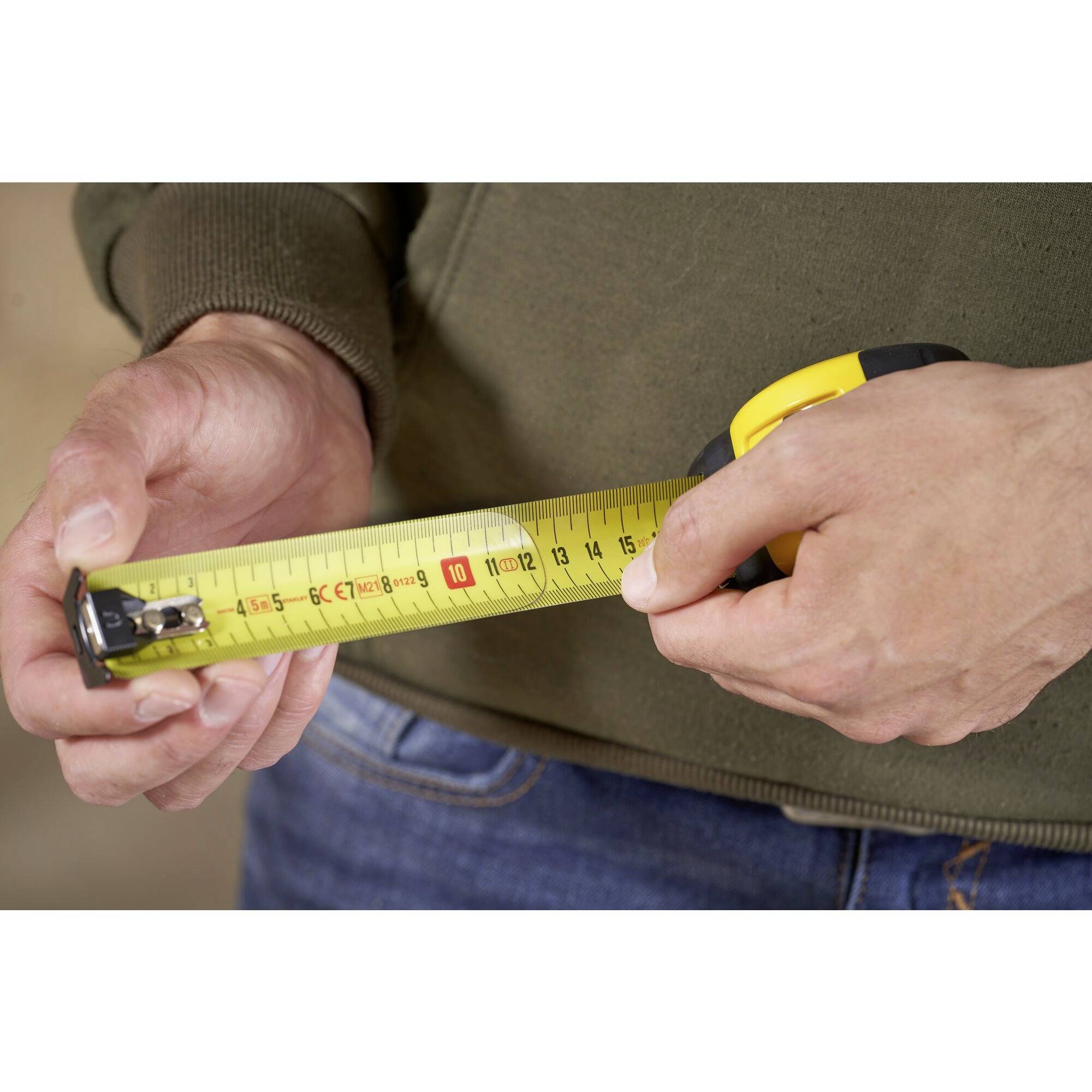 Osoba trzyma rozłożoną miarkę, wskazując na znacznik 10-centymetrowy, prawdopodobnie w celu dokładnego pomiaru lub wykonania prac rzemieślniczych.