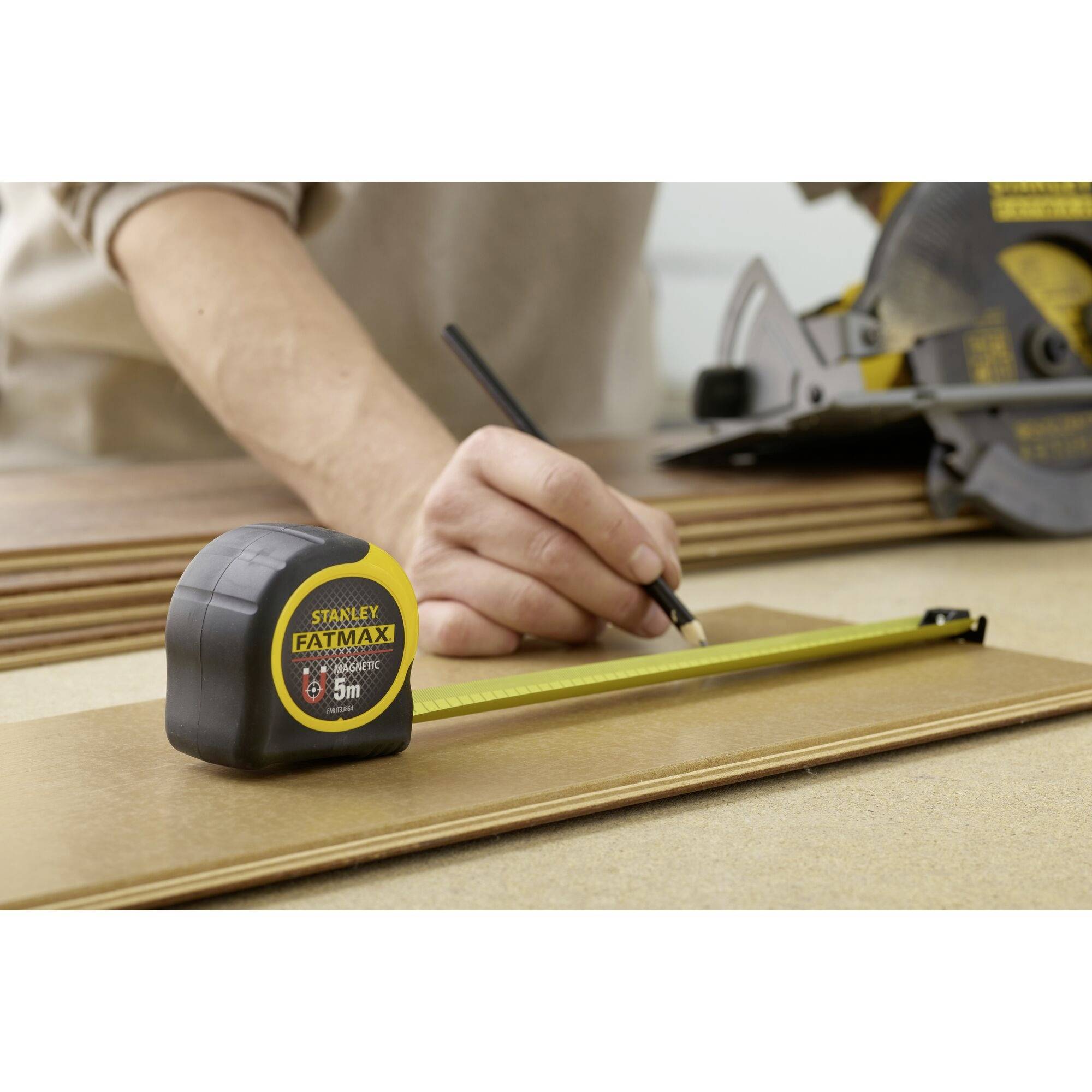 Osoba kreśli linie na desce za pomocą miarki i ołówka. W tle widać piłę tarczową.