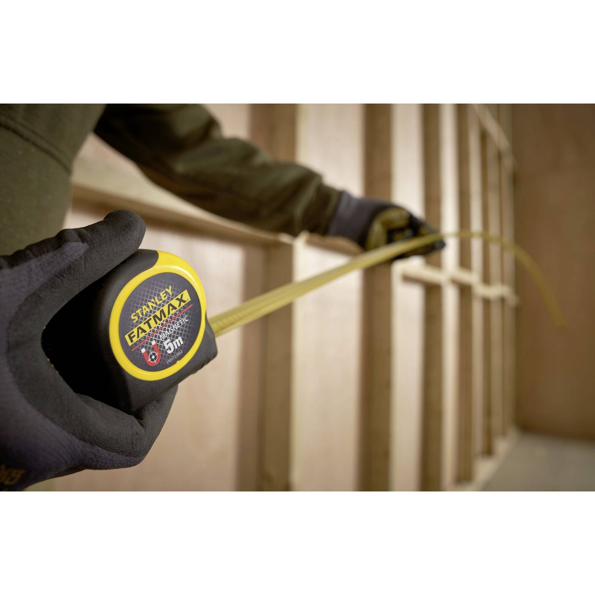 Osoba wyciąga miarkę z obudowy, aby dokonać pomiarów przy drewnianej ścianie szkieletowej.