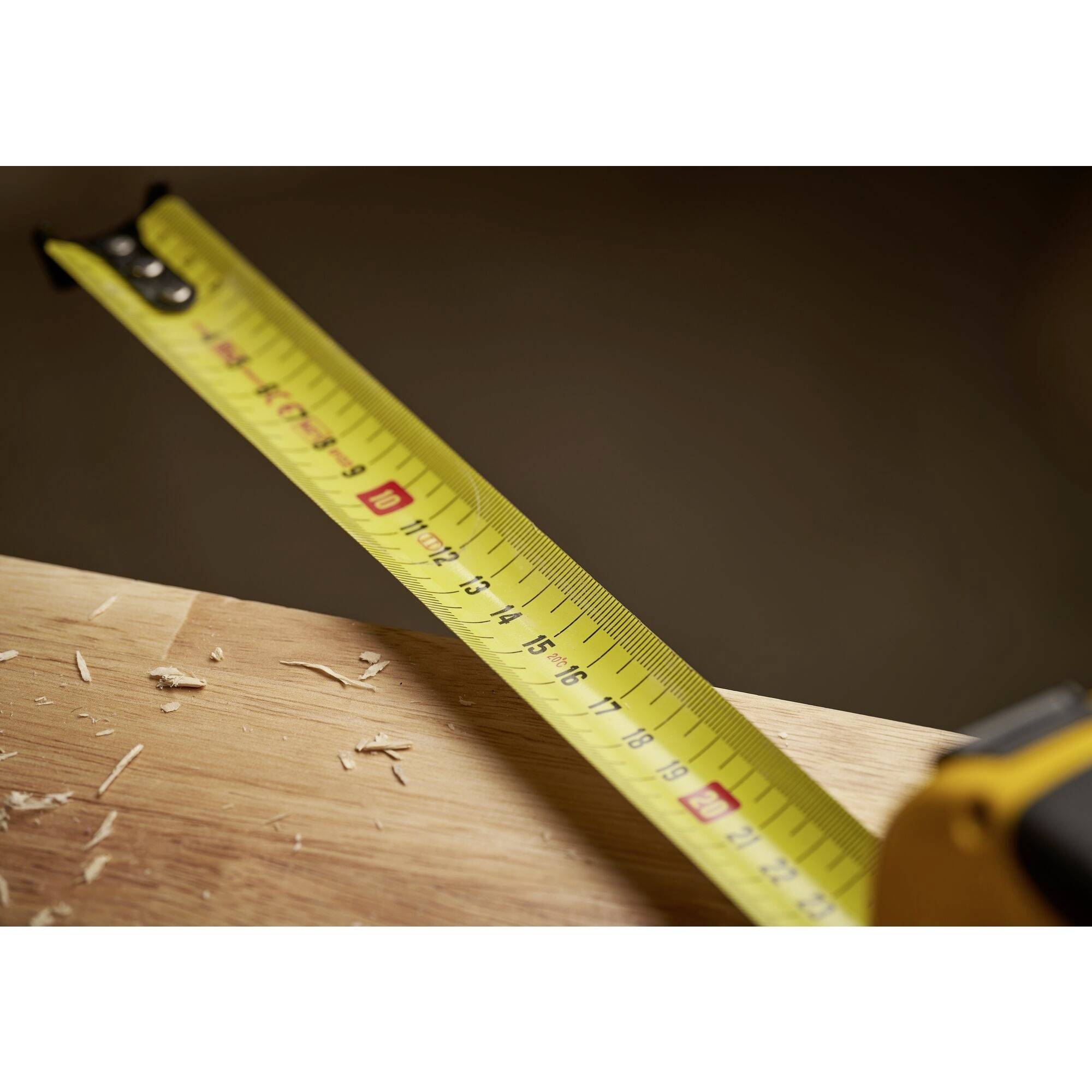 Żółta miarka leży na drewnianym stole z wiórami, prezentując precyzję pomiarów i rzemieślnicze mistrzostwo.