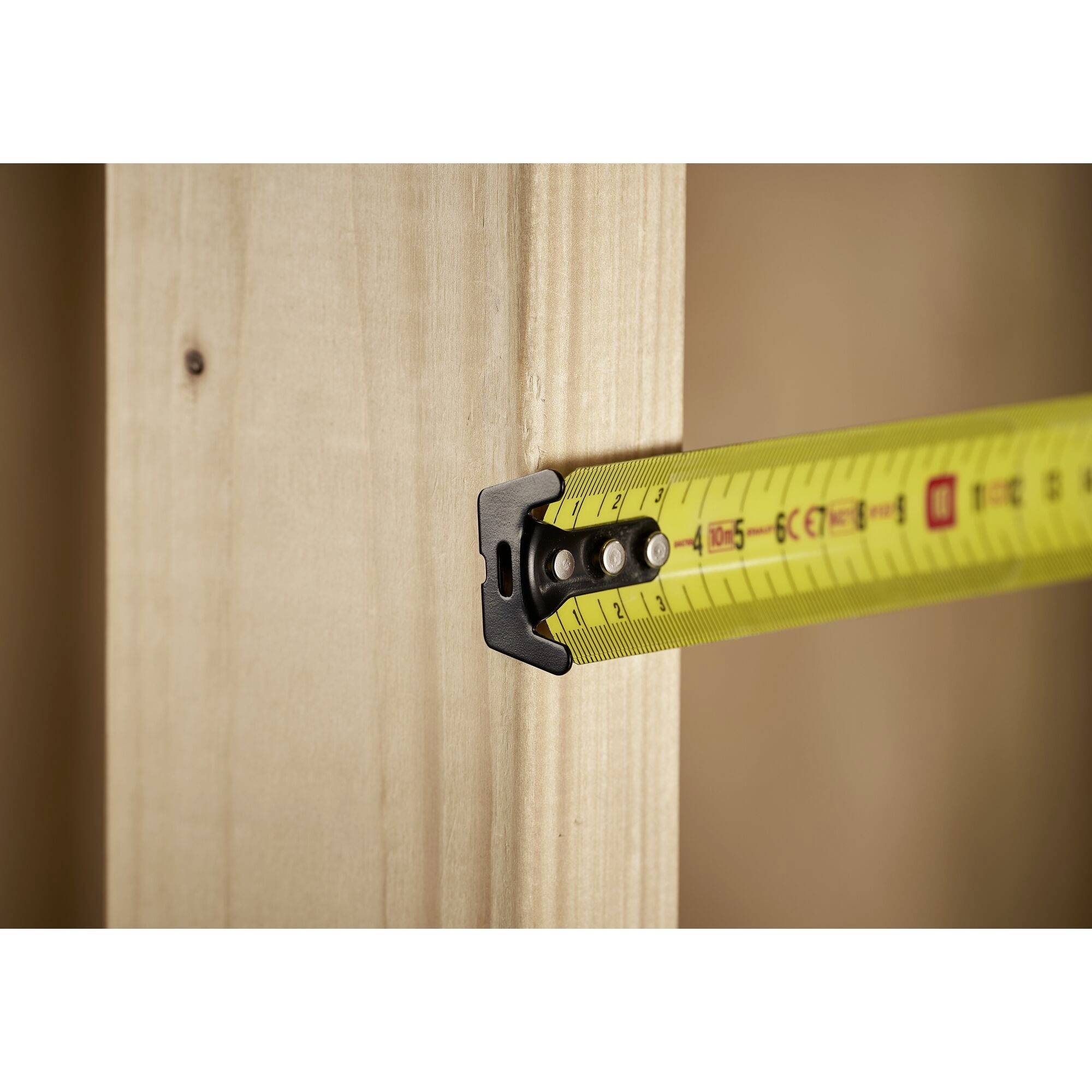 Żółta miarka mierzy odległość w drewnianej ramie.
