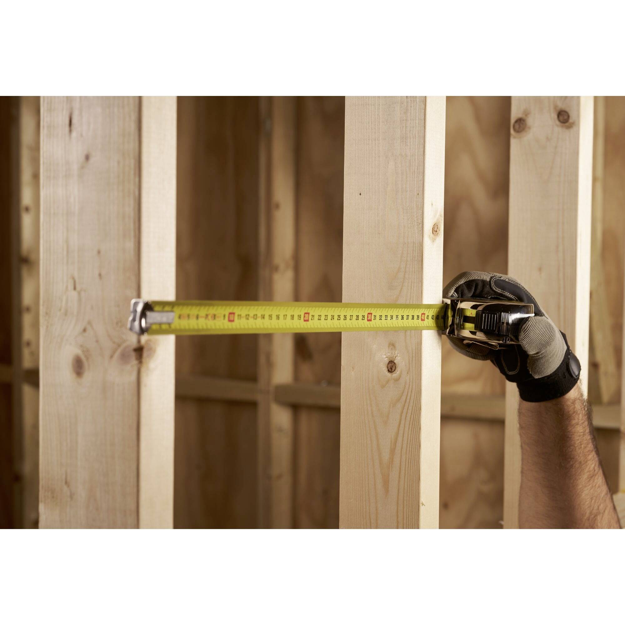 Rękawica trzyma miarkę przy drewnianej ramie. Miarka mierzy odległość między dwoma pionowymi deskami.