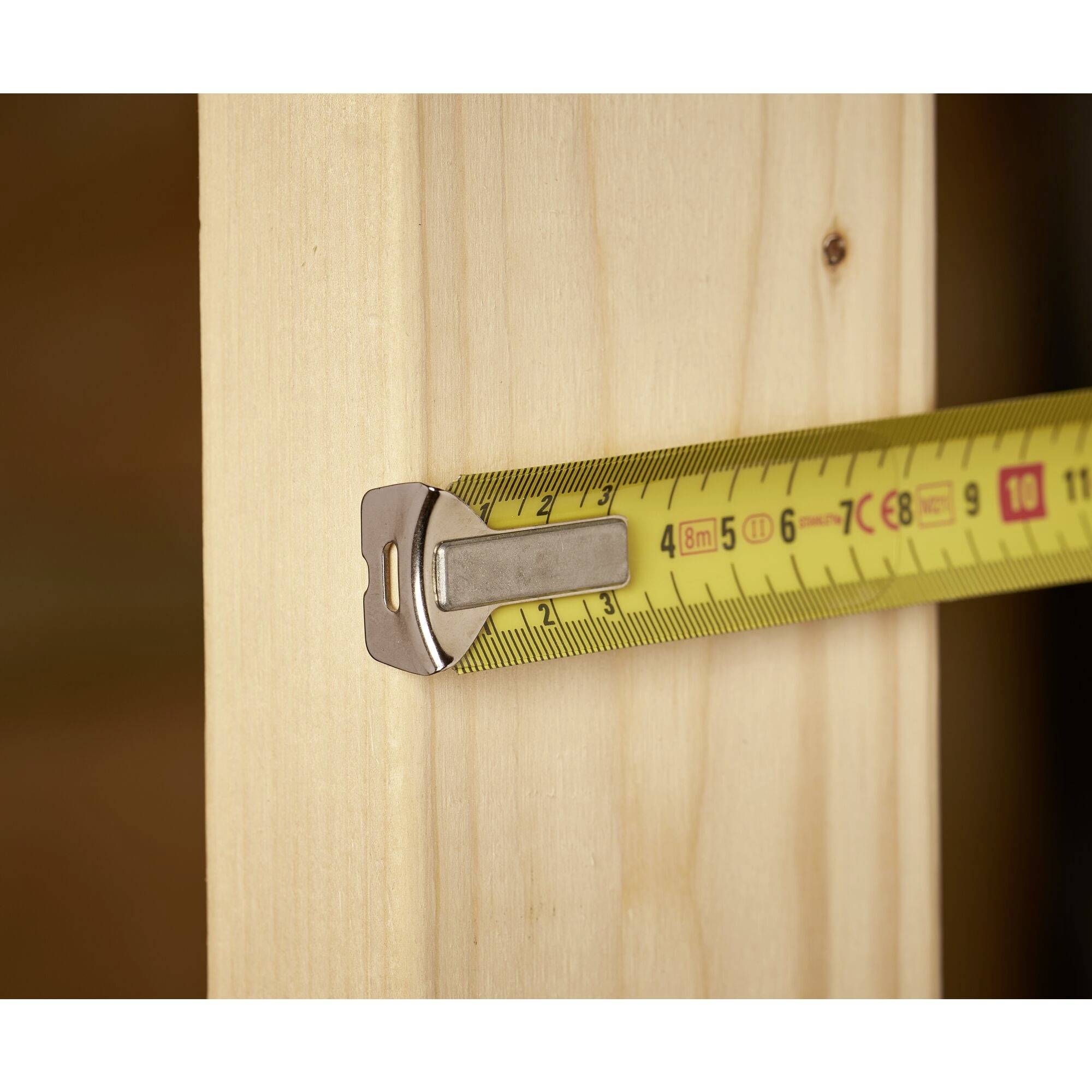 Żółta miarka mierzy szerokość deski drewnianej, wskazując 10 cm.