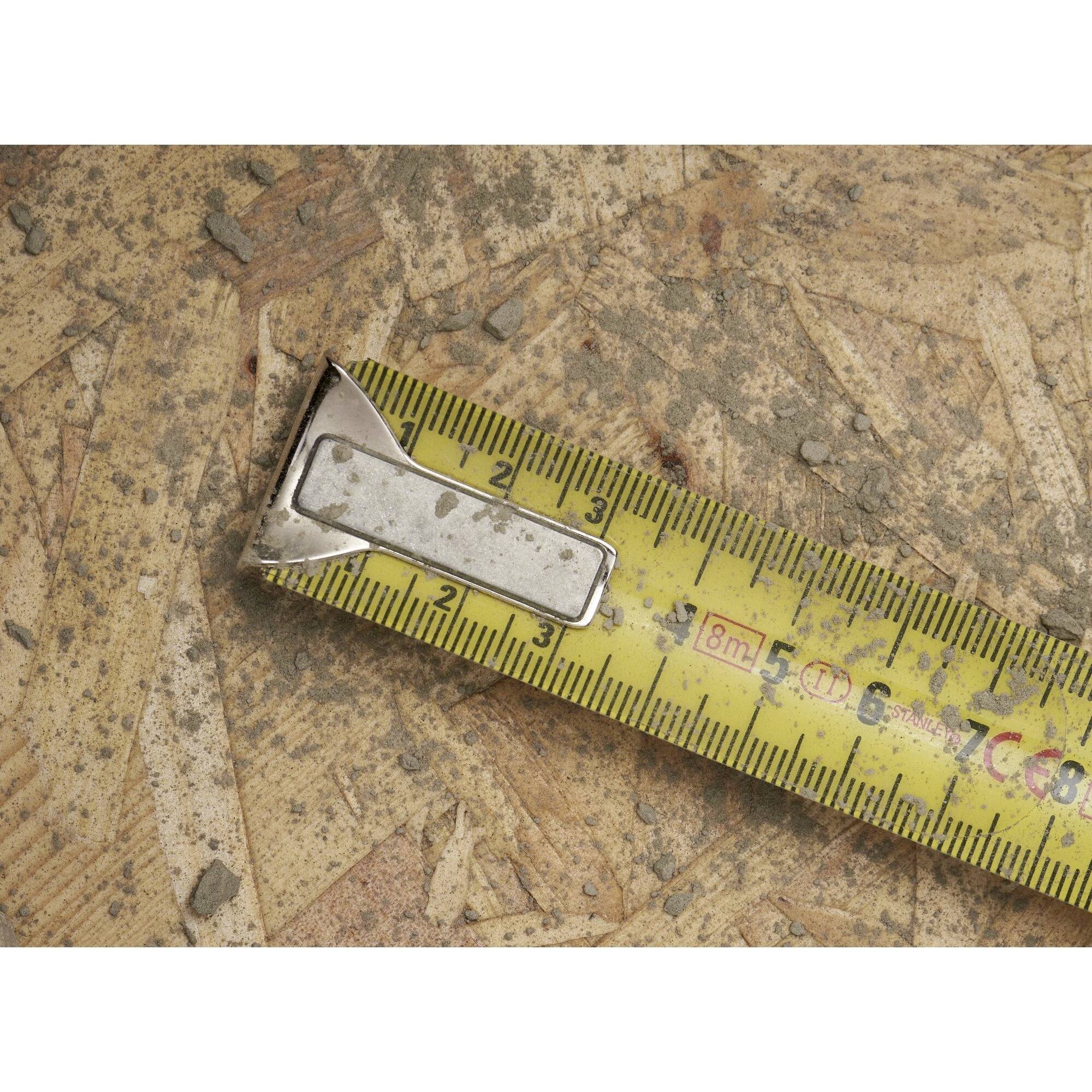 Żółta miarka leży na zniszczonej powierzchni wykonanej z płyty wiórowej. Taśma pokazuje numer '2'.