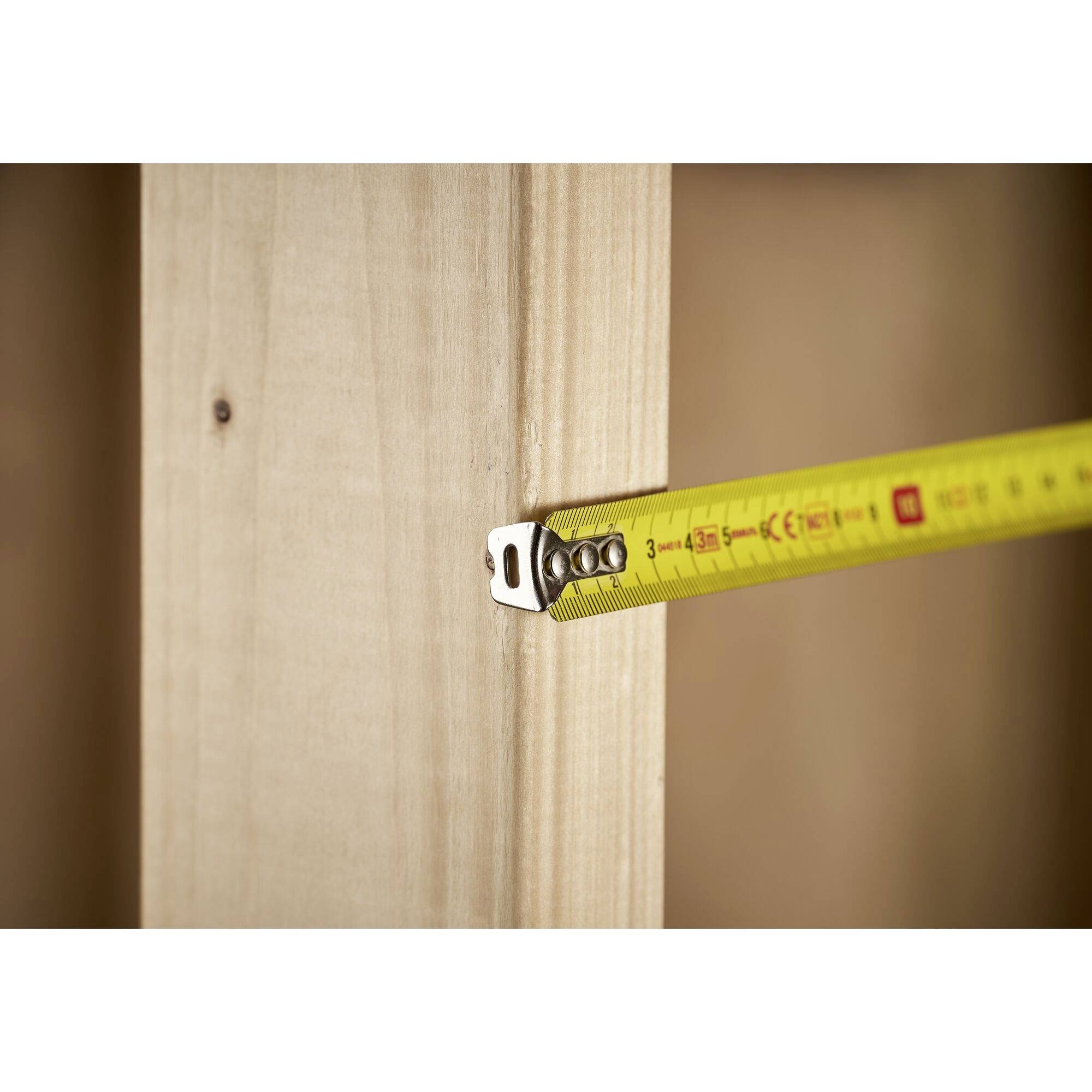 Żółta miara krawiecka mierzy głębokość drewnianej półki przedstawionej w widoku pionowym. Wskazuje ona około 3,7 cm.