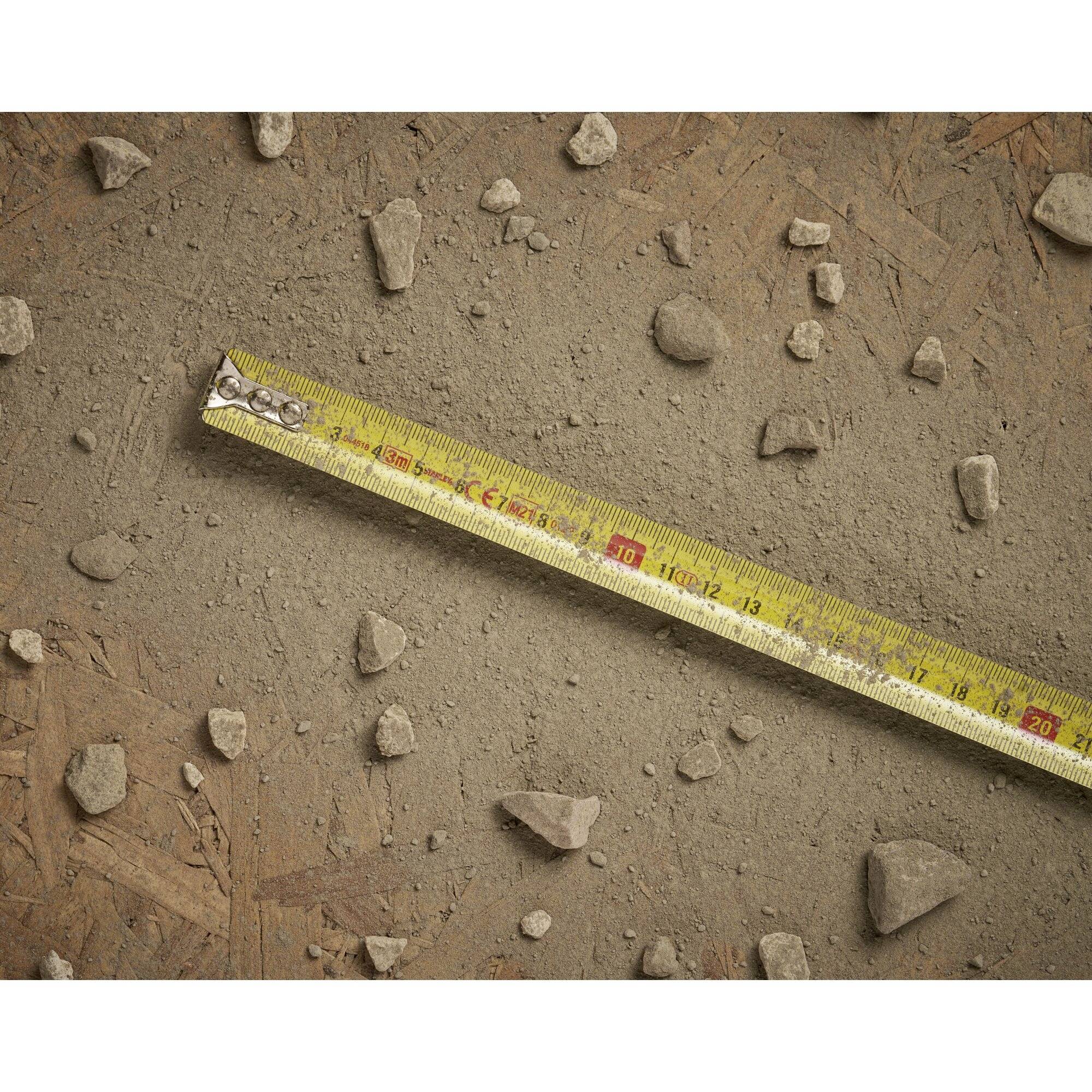 Żółta miarka leży ukośnie na ziemistym podłożu z małymi kamieniami.