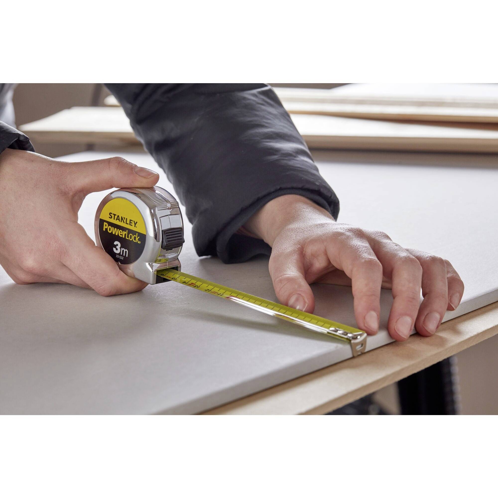 Osoba mierzy deskę drewnianą za pomocą taśmy mierniczej.