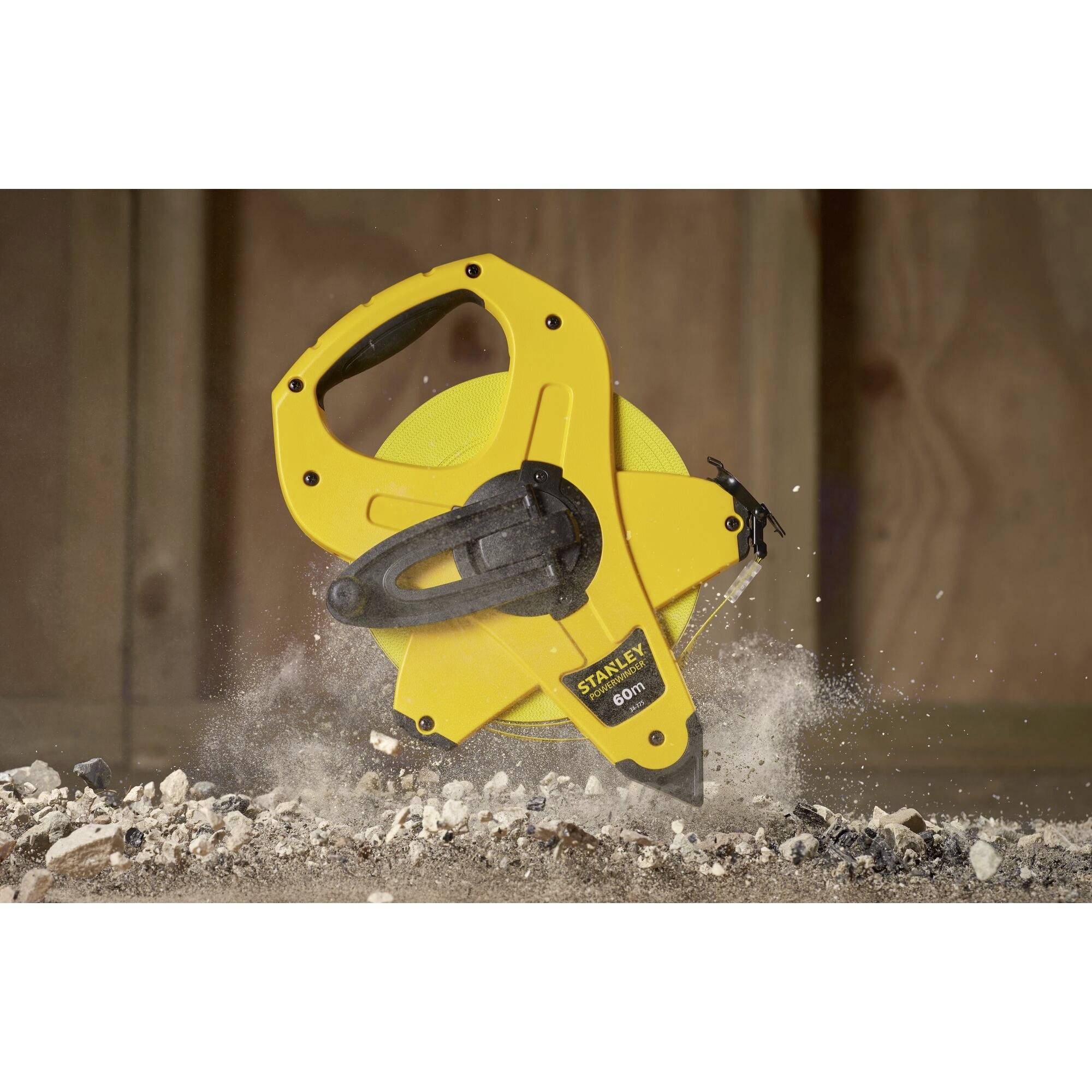 Żółta, stabilna taśma miernicza leżąca na podłożu żwirowym i pylistym, nadająca się do precyzyjnych pomiarów w środowisku budowlanym.