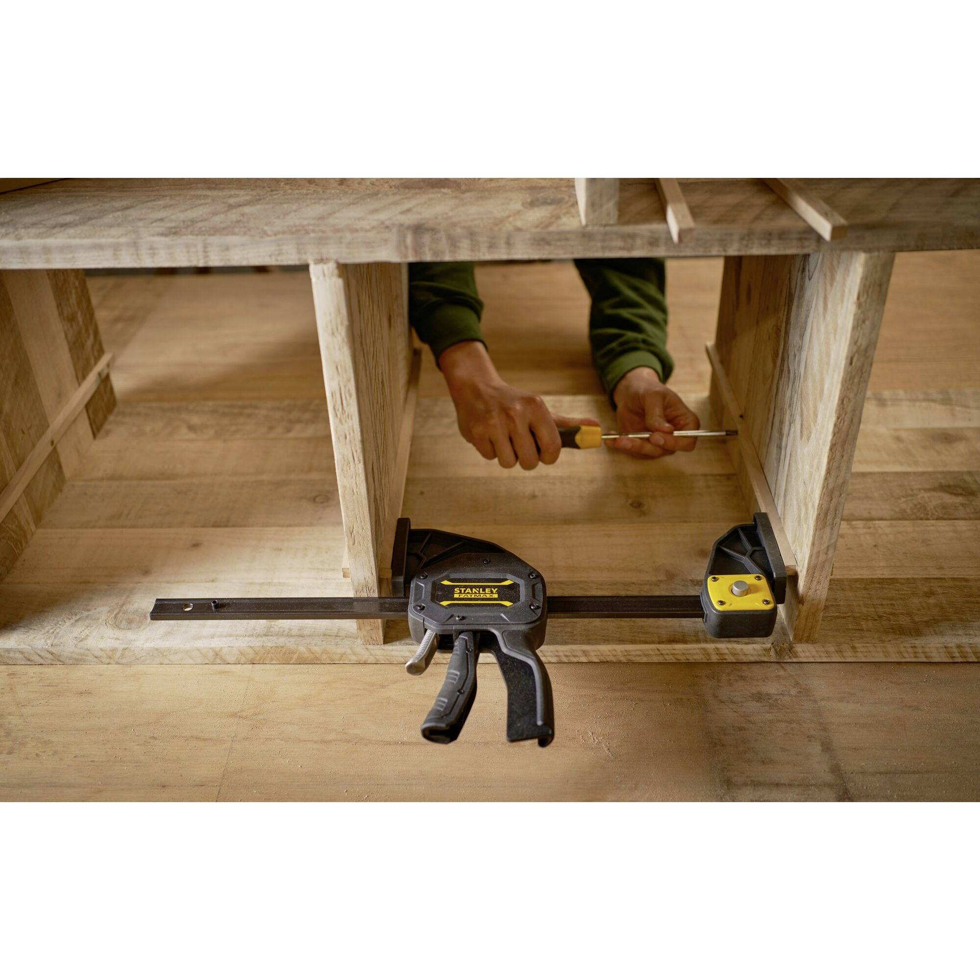 Osoba mocuje element drewniany śrubokrętem, jednocześnie używając zacisku do stabilizacji.