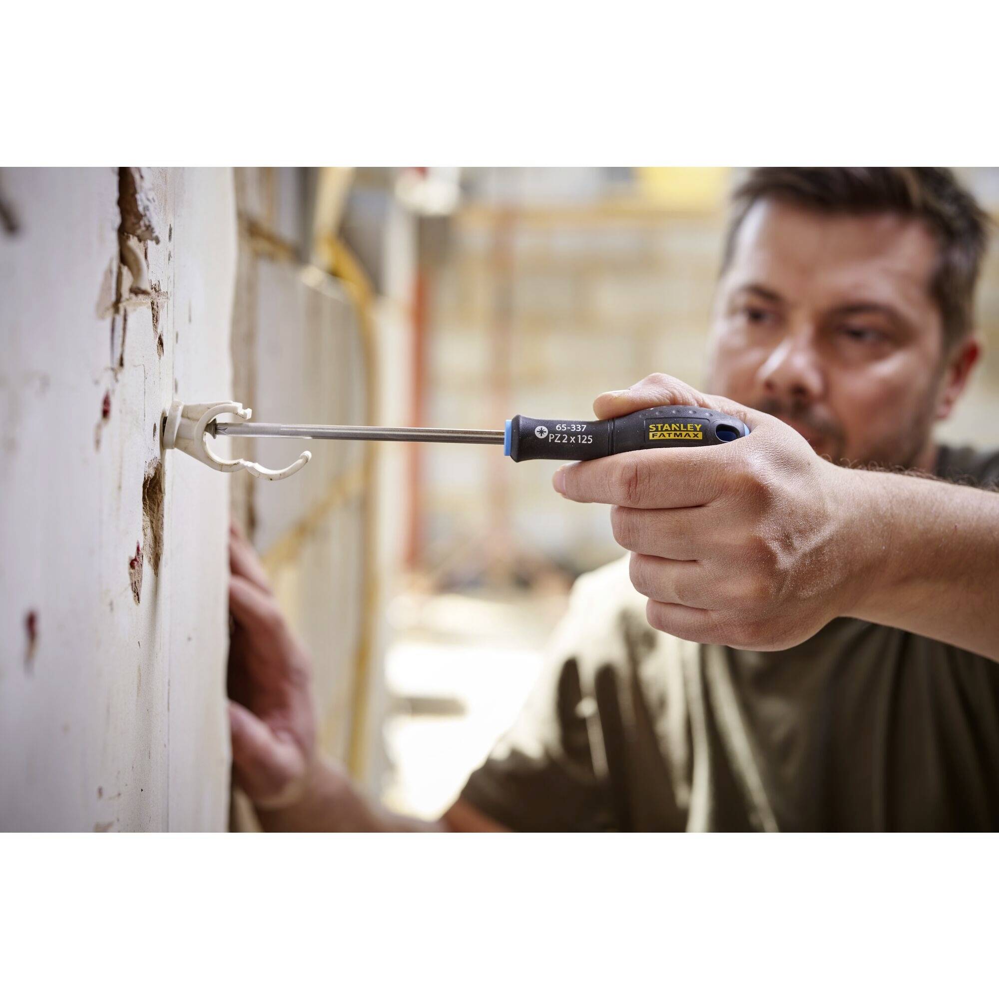 Osoba używa śrubokręta, aby wywiercić otwór w ścianie. Fokus jest skierowany na dłoń i narzędzie.