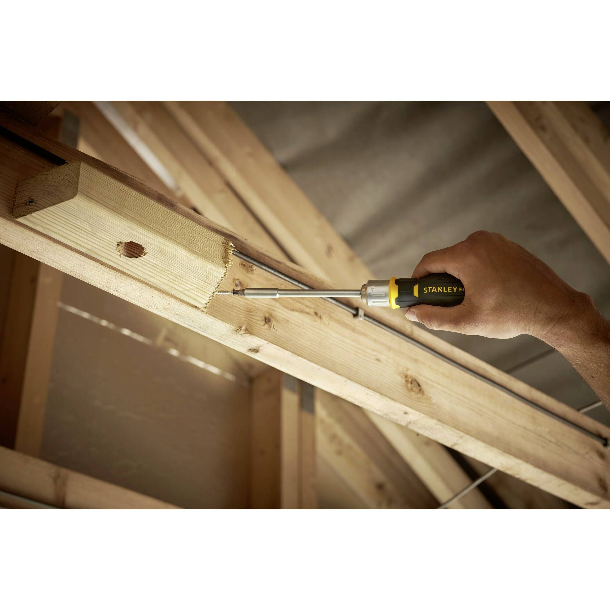 Wkrętak wkręca wkręt drewniany w drewniany balken w poddaszu. Jedna ręka mocno trzyma wkrętak.