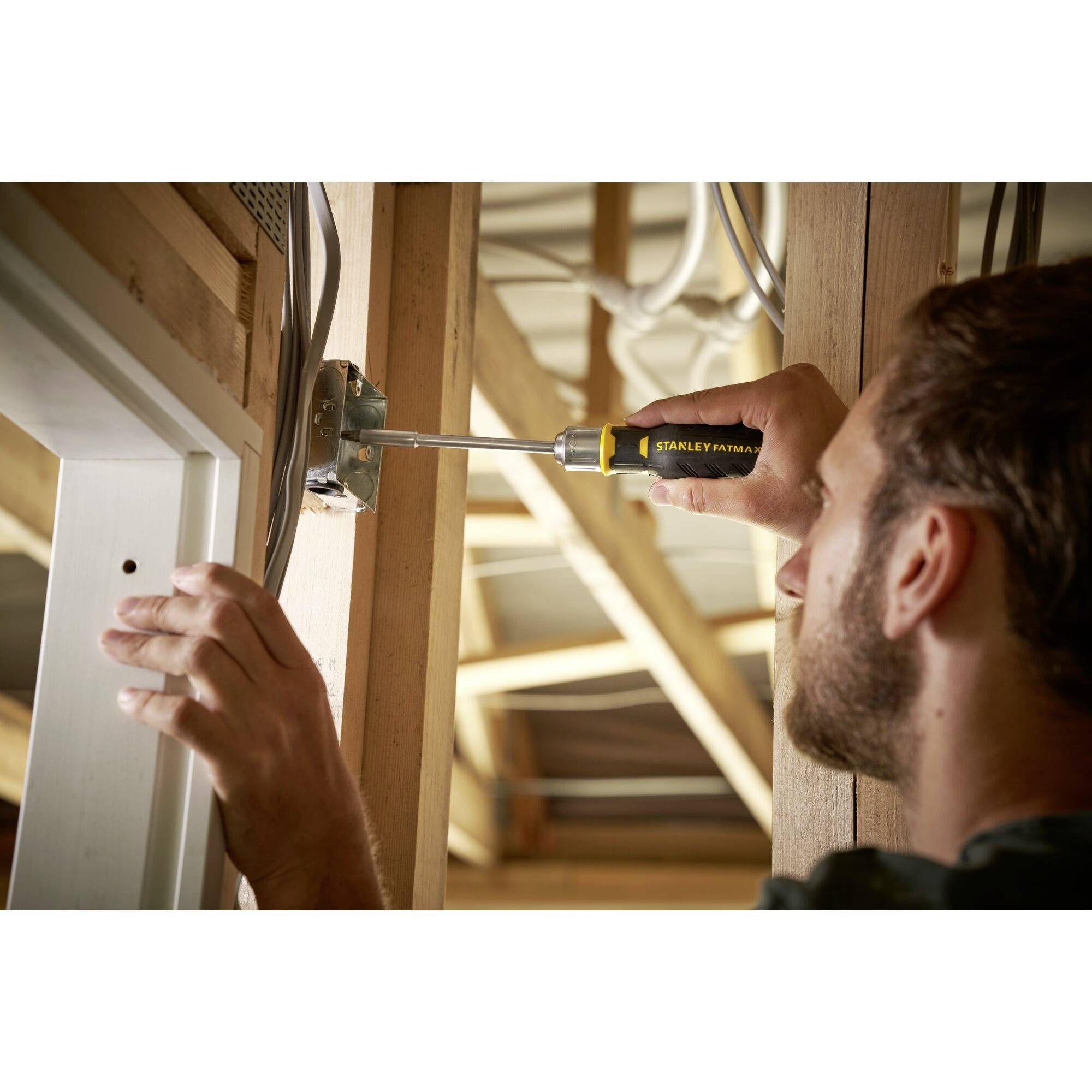 Mężczyzna przykręca gniazdko elektryczne w drewnianej ramie domu za pomocą wkrętaka.