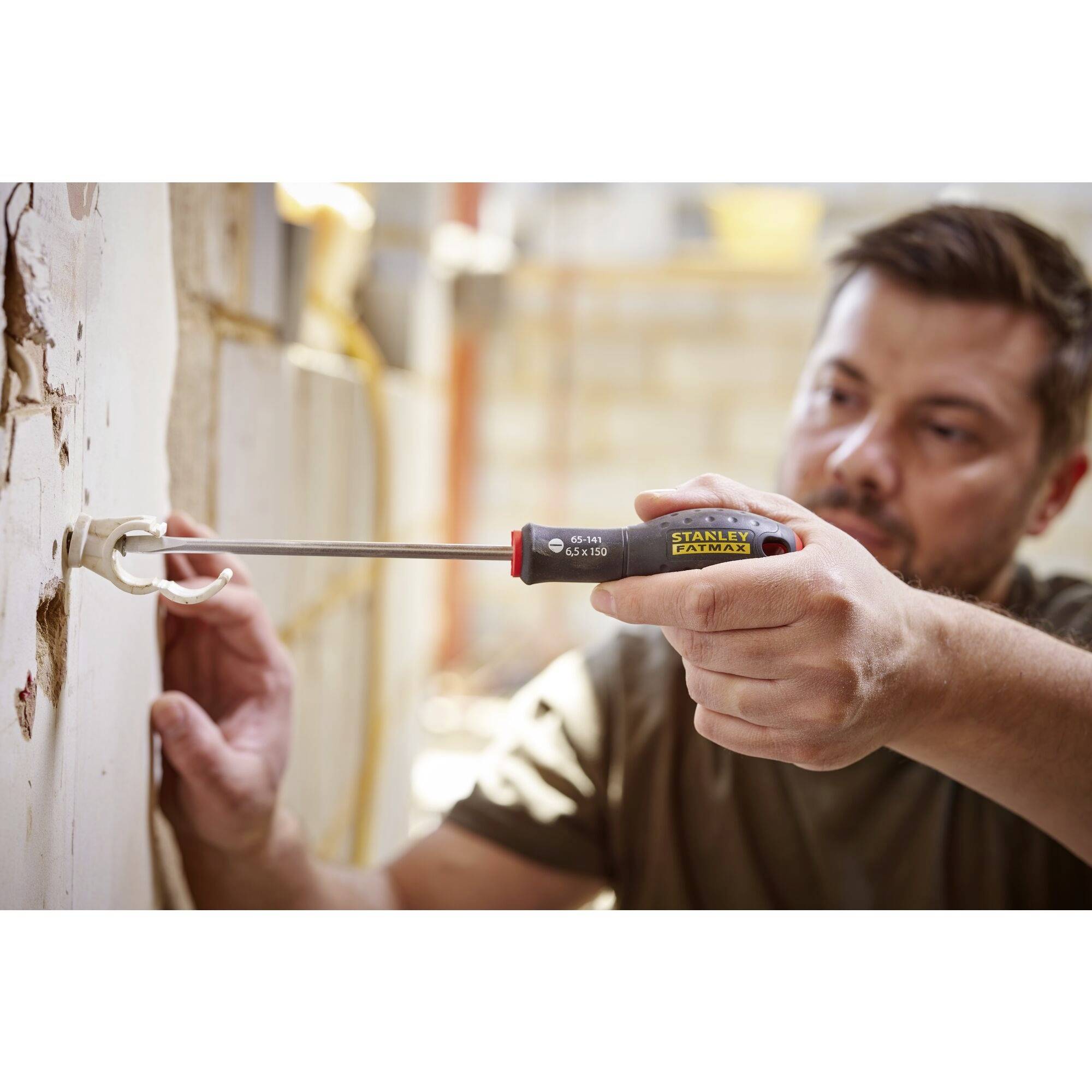 Mężczyzna naprawia gniazdko elektryczne za pomocą śrubokręta. W tle widać rozmyte zaplecze budowy.