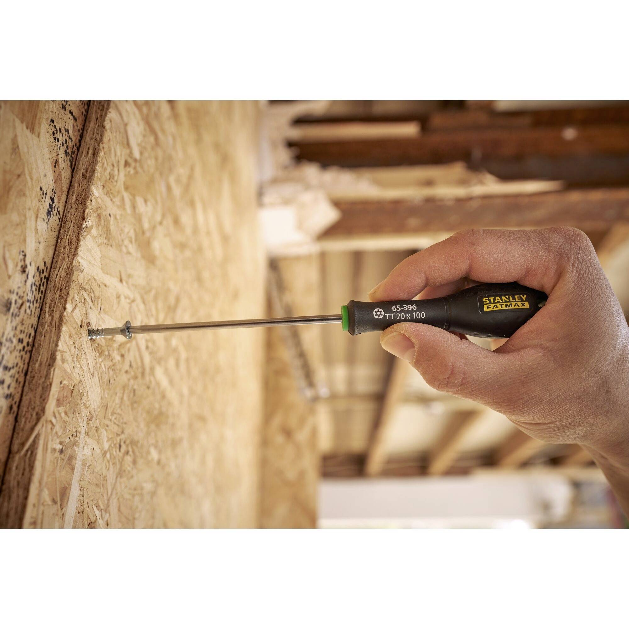 Ręka wkręca wkręt wkrętakiem w drewnianą płytę. W tle widoczna jest niekompletna drewniana konstrukcja.