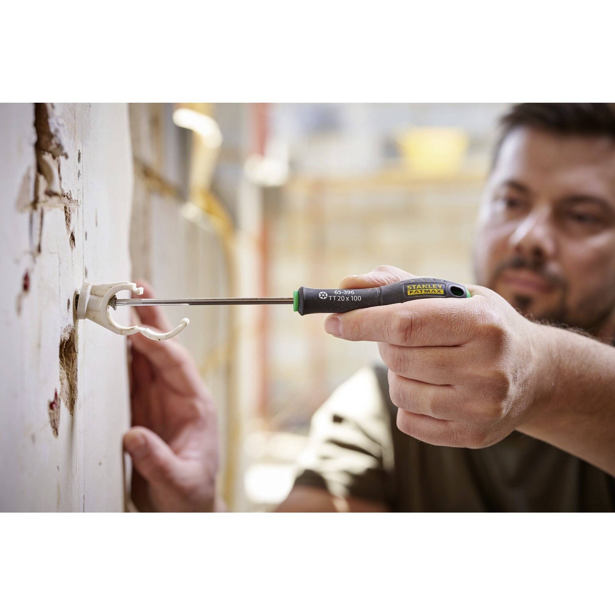 Mężczyzna instaluje gniazdko elektryczne w ścianie. Trzyma śrubokręt i dokręca śruby.