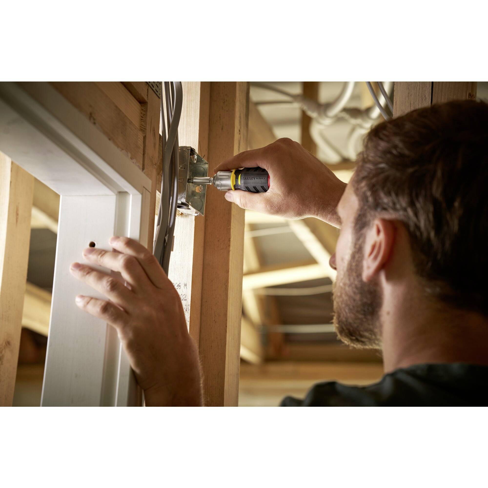 Osoba przytwierdzająca śrubokrętem elektryczną płytę do drewnianej ramy w niedokończonym pomieszczeniu.