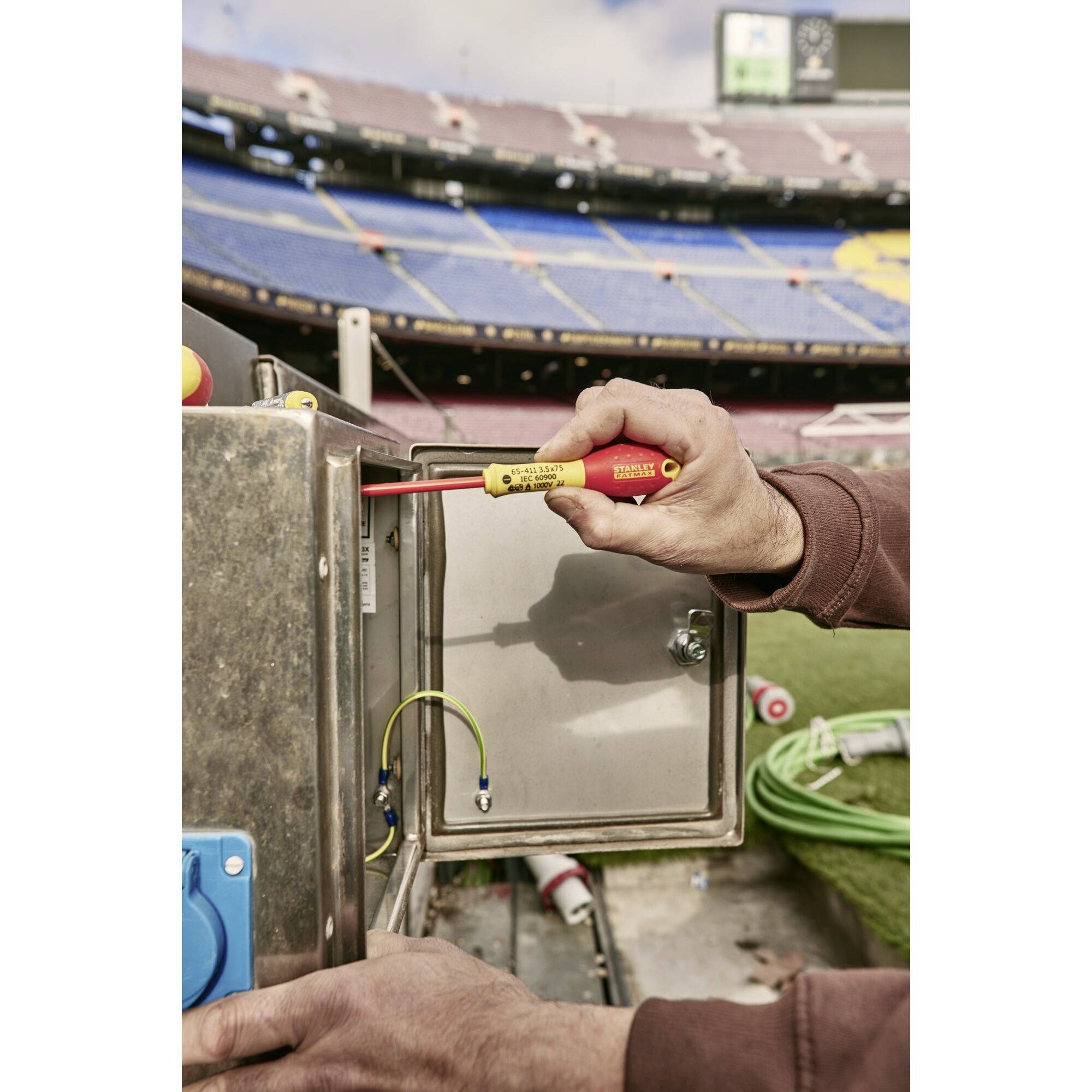 Jedna osoba pracuje z miernikiem elektrycznym przy rozdzielnicy elektrycznej na pustym stadionie.
