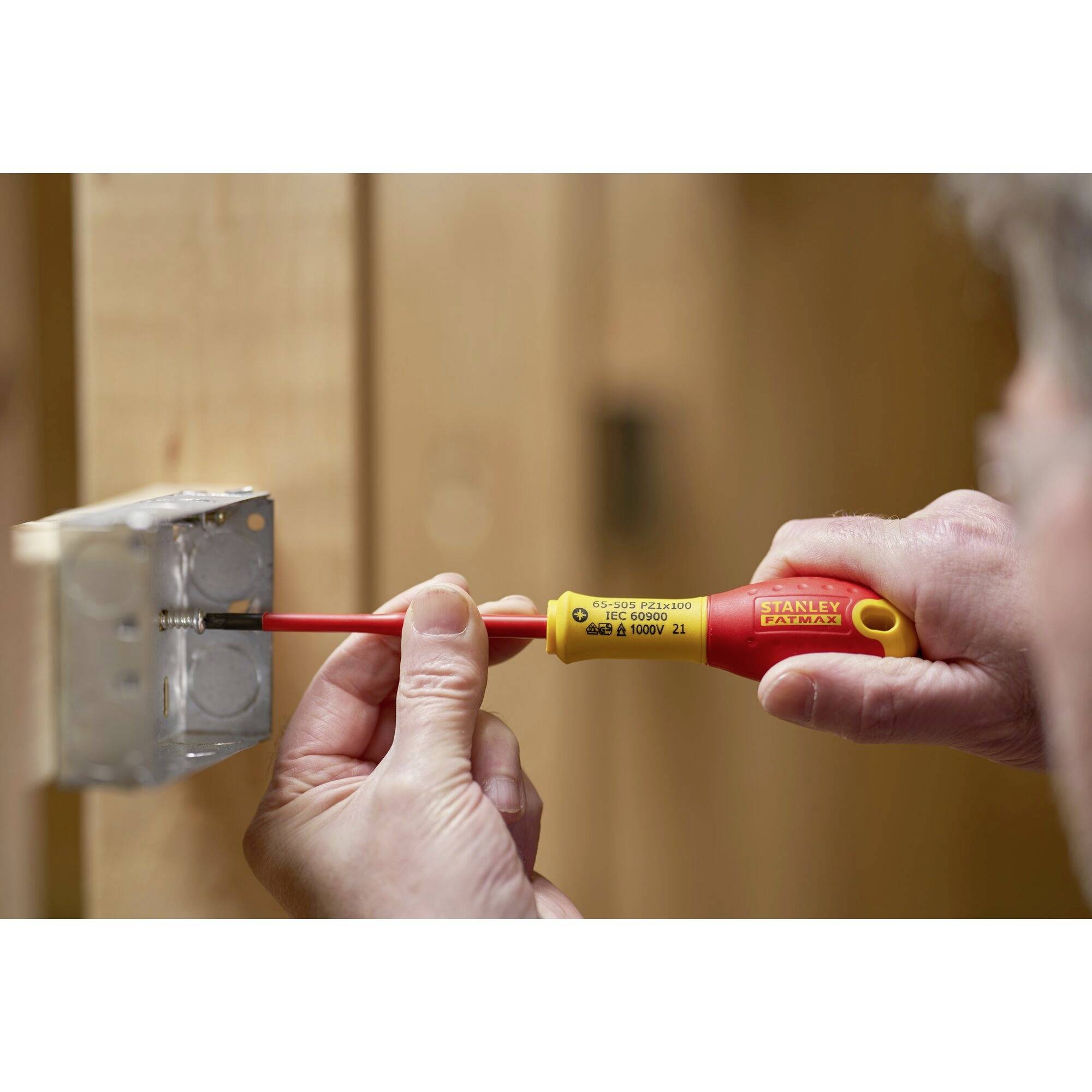 Osoba wkręca śrubę w metalową puszkę elektryczną za pomocą izolowanego wkrętaka.