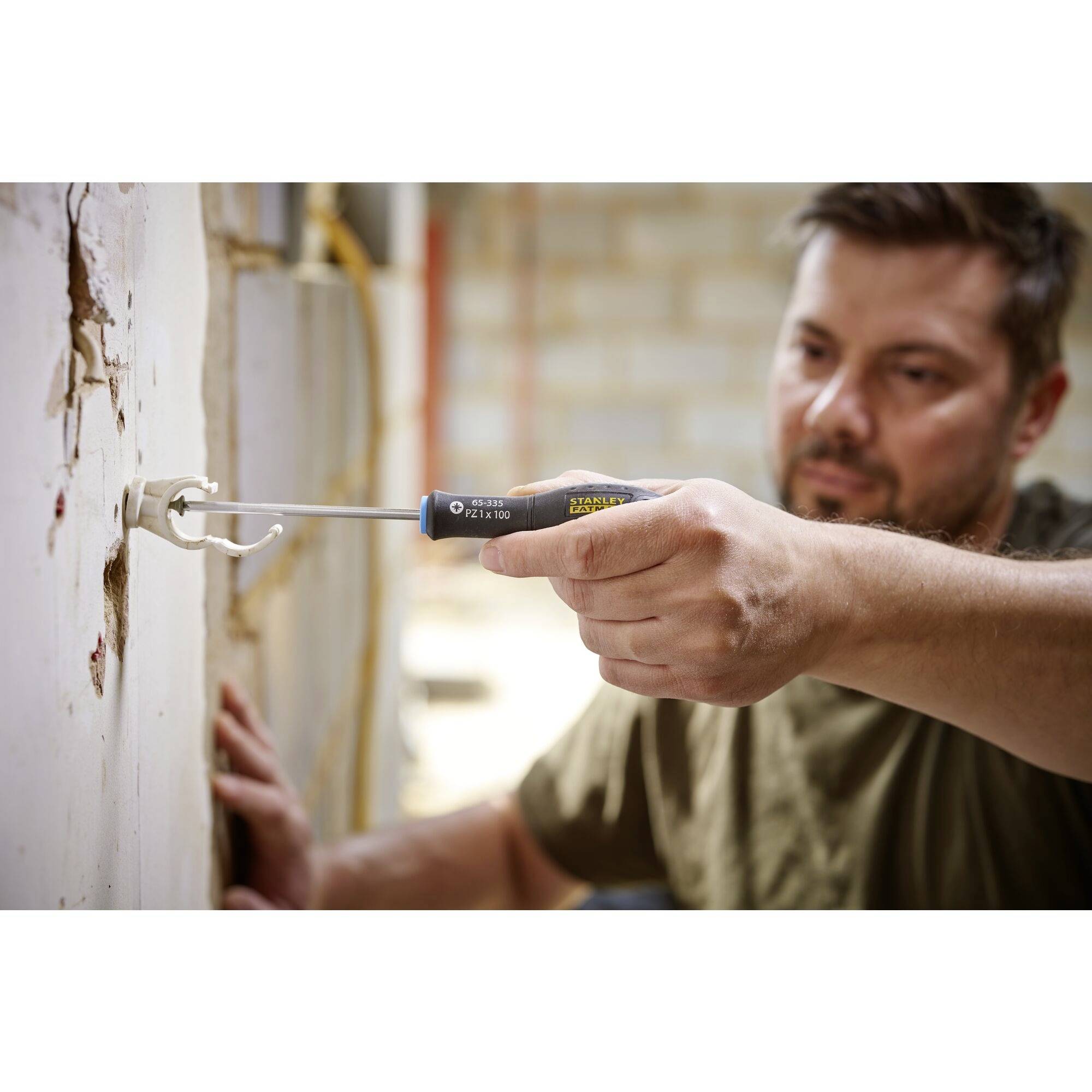 Mężczyzna naprawia gniazdko elektryczne śrubokrętem w niedokończonym pomieszczeniu.