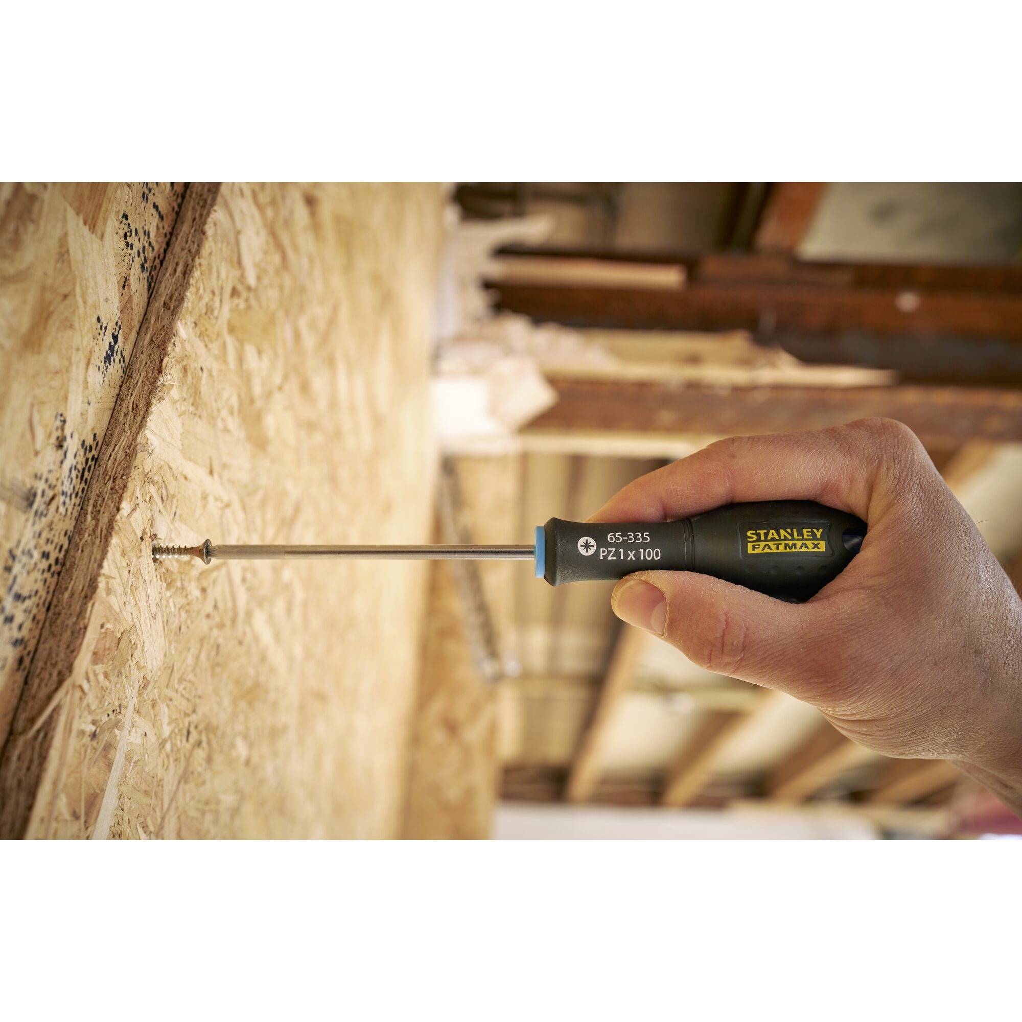 Ręka trzyma śrubokręt i wkręca śrubę w drewnianą ścianę.