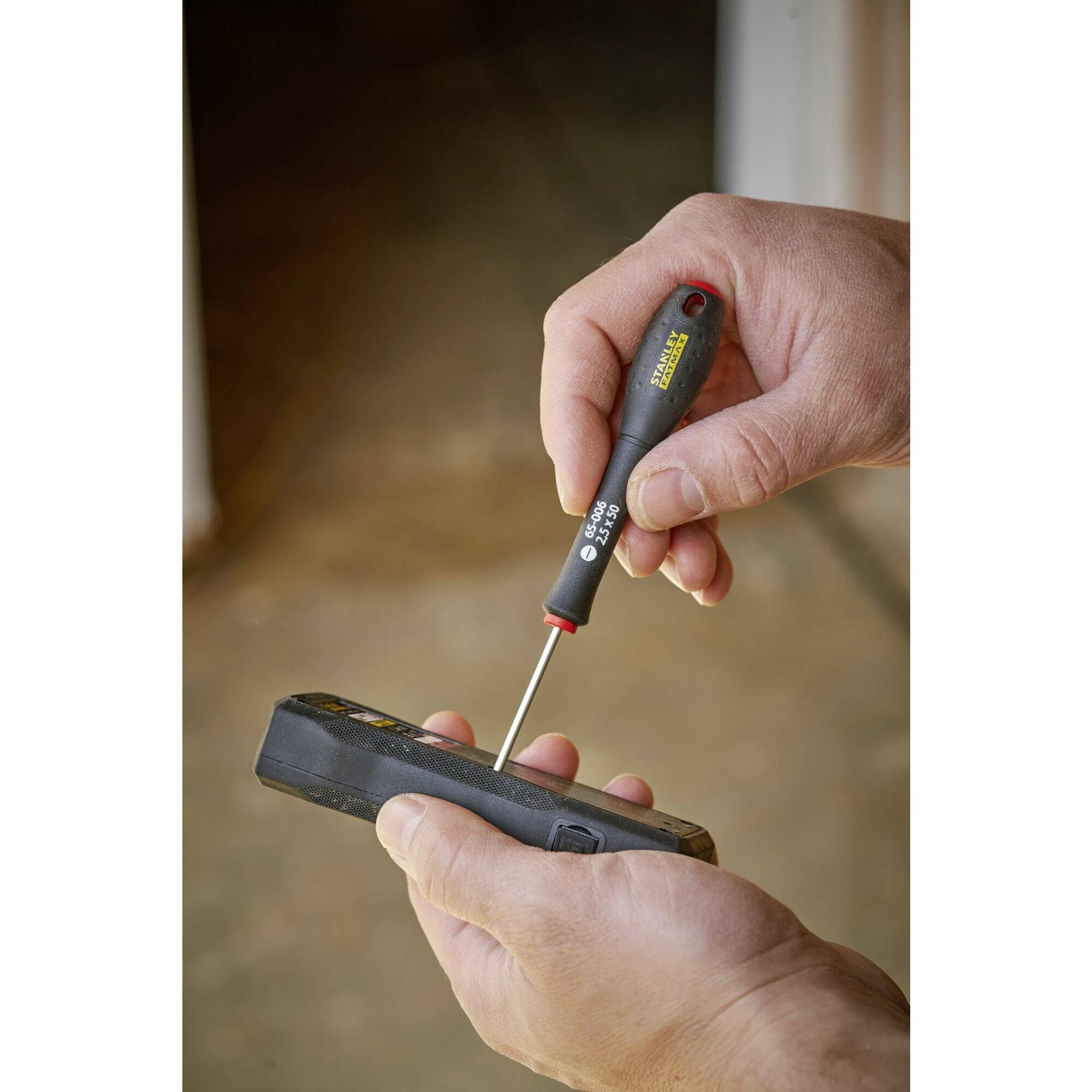 Osoba trzyma czarny śrubokręt i używa go do otwarcia lub naprawy urządzenia elektronicznego.