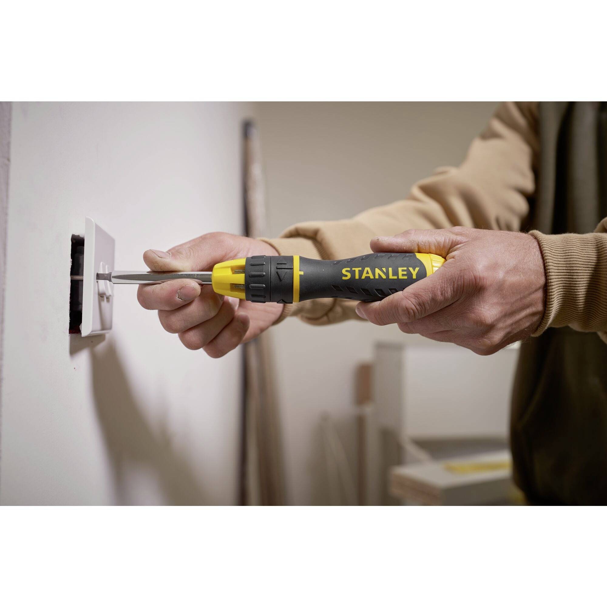 Osoba używa śrubokręta do zamontowania gniazdka elektrycznego na ścianie. Ręce i narzędzie są w centrum uwagi.