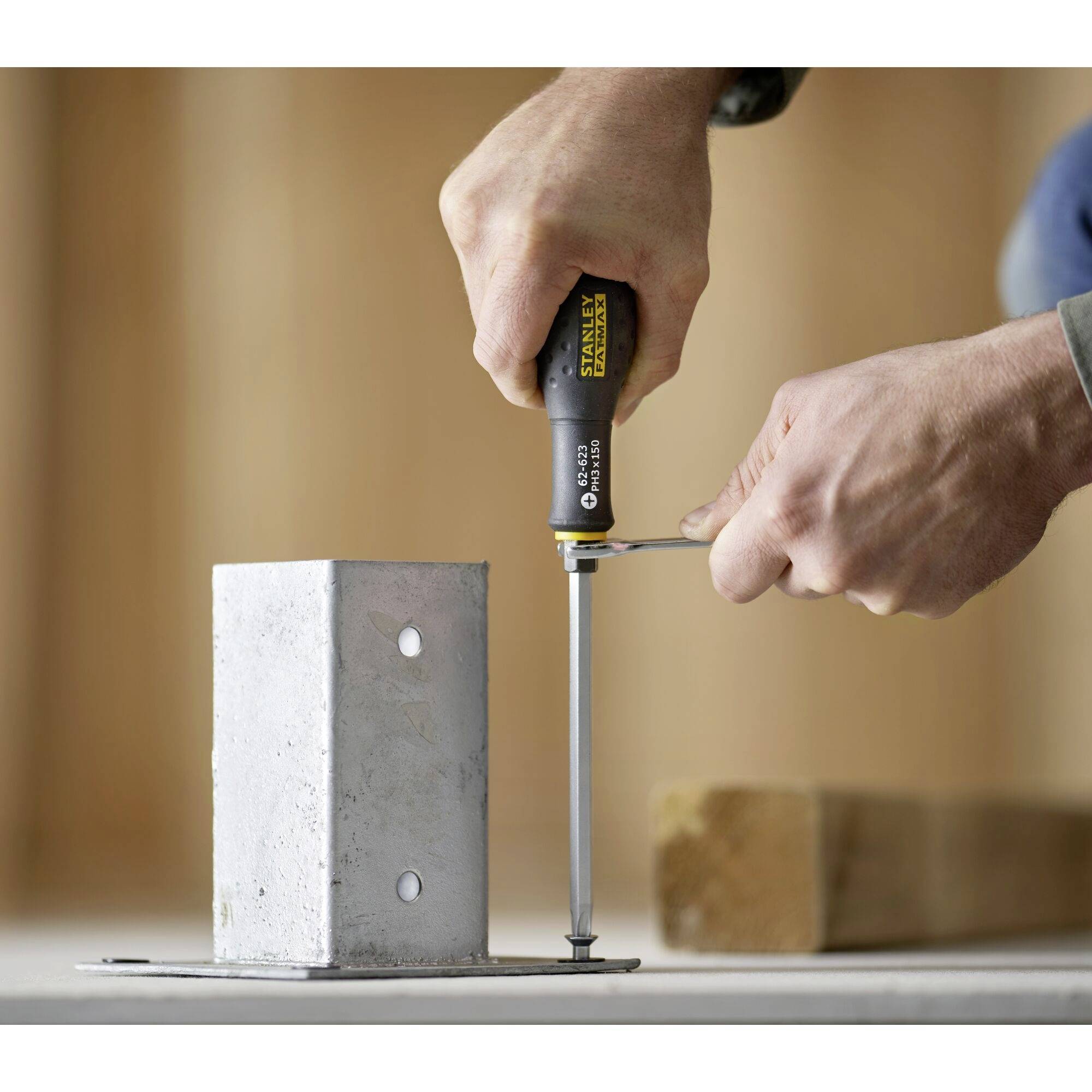 Osoba dokręca wkręt śrubokrętem w metalowy uchwyt. Fokus na dłoni i narzędziu.