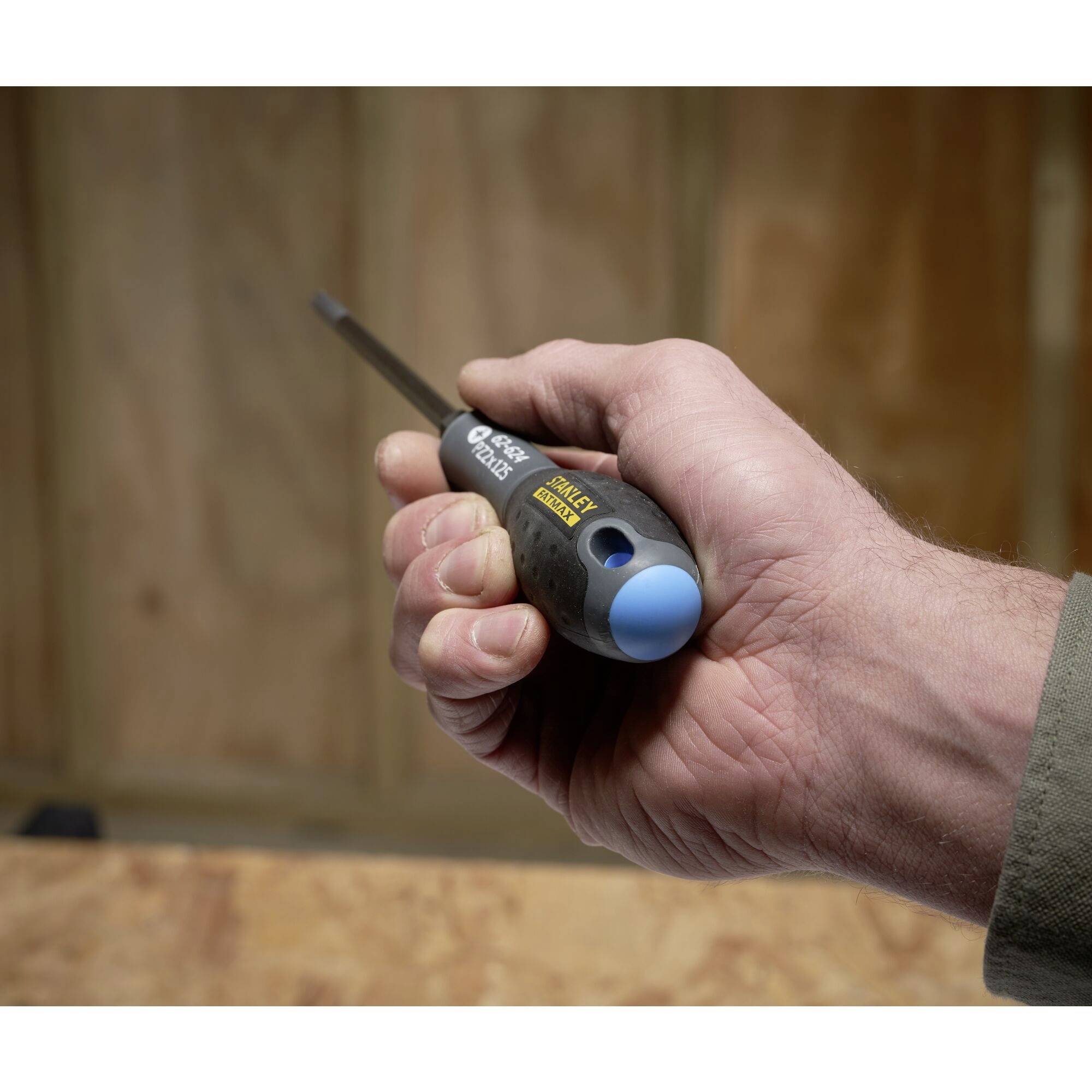 Dłoń trzyma śrubokręt z niebieskim czubkiem i czarną rękojeścią na tle drewnianego podłoża.