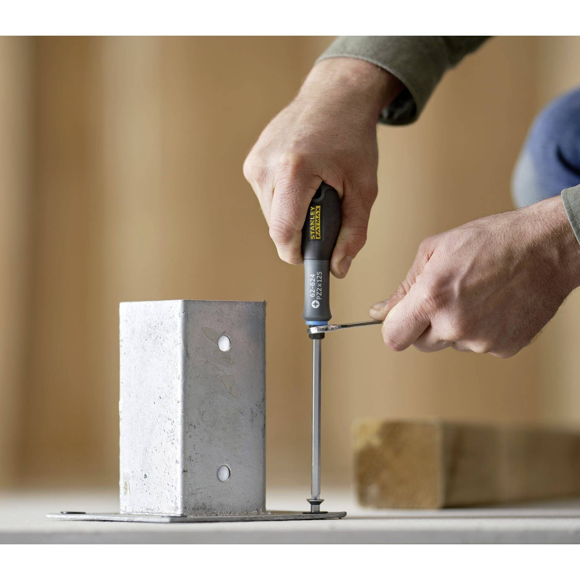 Osoba wkręca śrubę wkrętakiem w kawałek metalu. Ręce i narzędzie są w centrum uwagi, tło rozmyte.