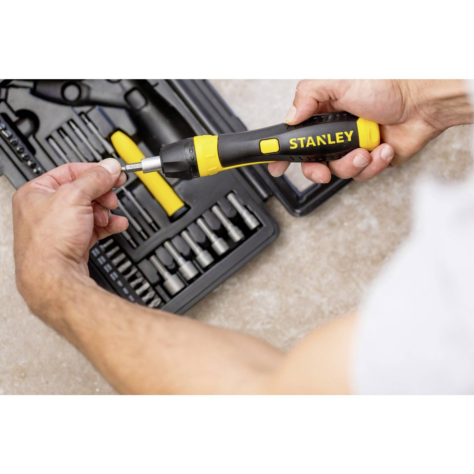 Osoba trzyma żółty wkrętak marki Stanley nad otwartą walizką narzędziową z różnymi końcówkami i narzędziami.