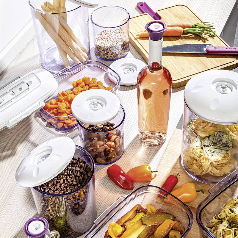 Pojemniki na zapasy z produktami spożywczymi: makaron, orzechy, marchewka i przyprawy. Akcesoria kuchenne i deska do krojenia z nożem obok.