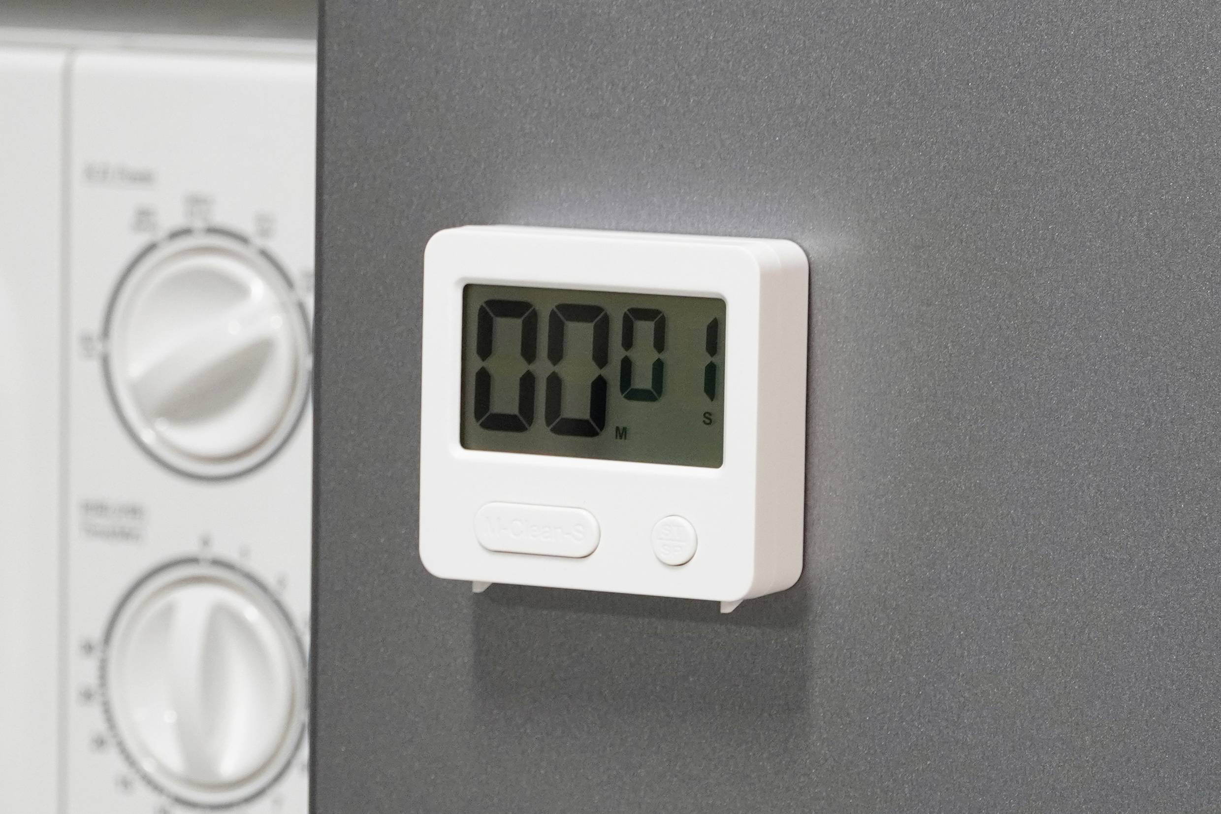 Cyfrowy minutnik kuchenny pokazuje '00:01'. Po prawej stronie widoczne są przyciski pralki lub piekarnika.